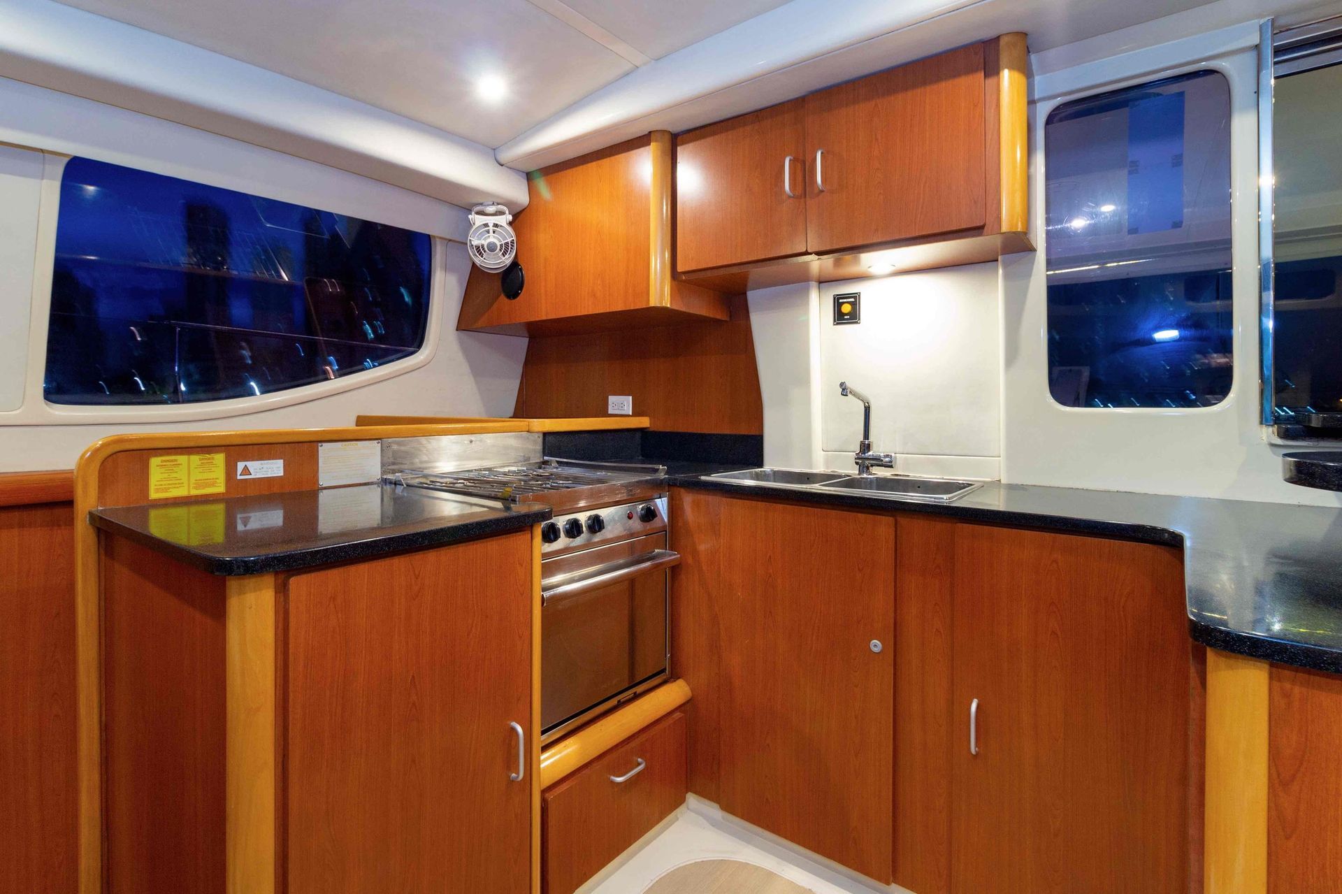 Interior view of a boat galley with wooden cabinetry, black countertops, and a stove. There are windows along the walls.
