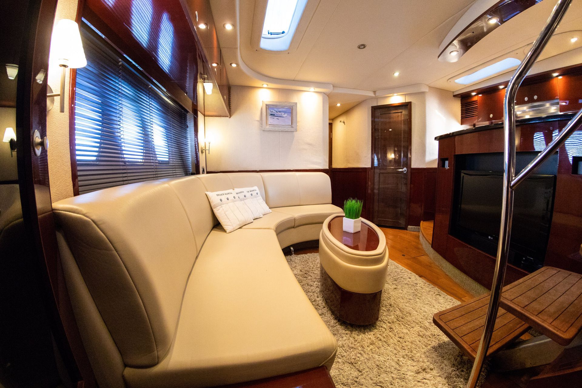 Interior of a yacht with curved cream couch, wooden accents, and a small table with a plant.
