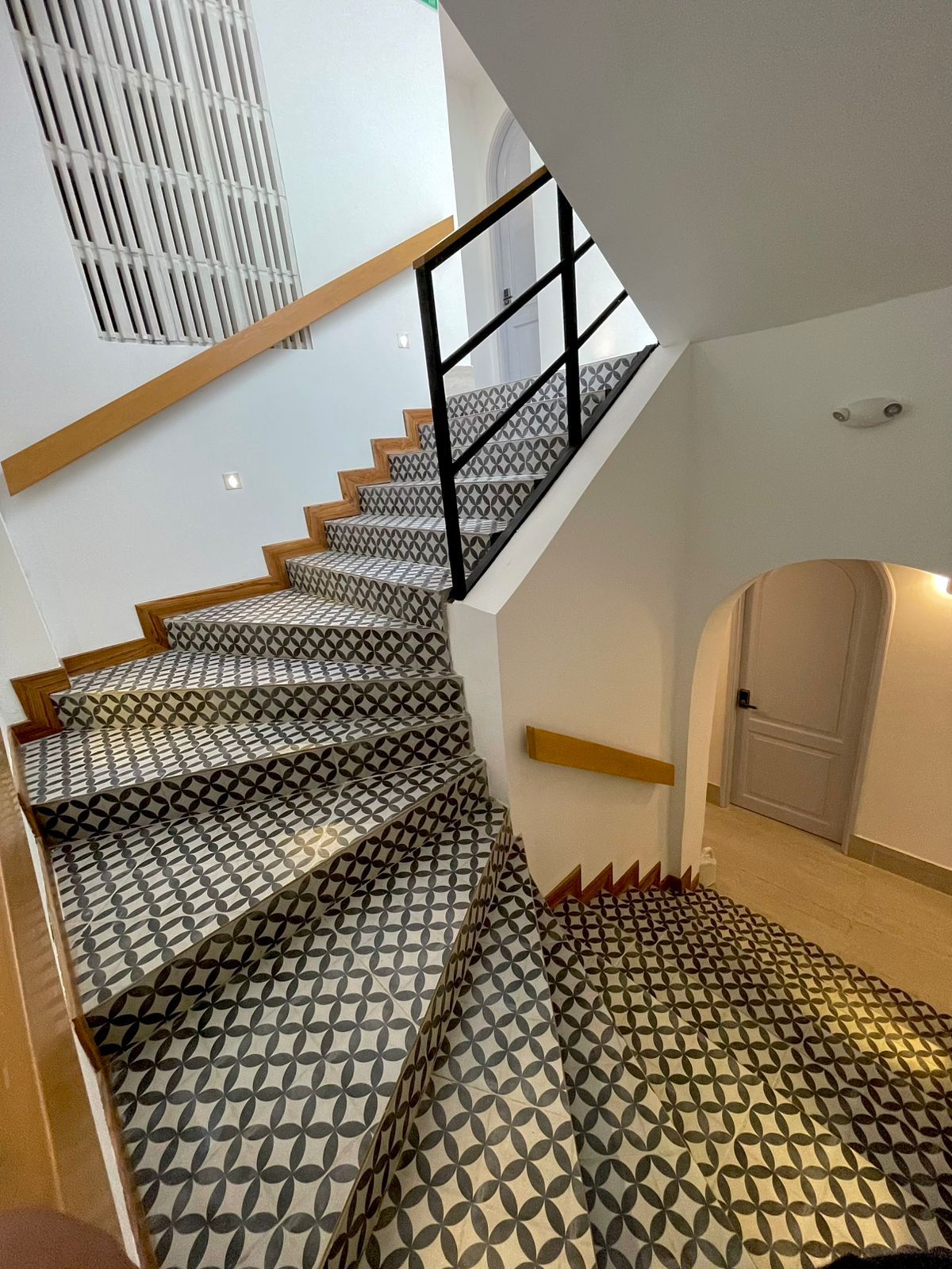 Staircase with patterned tile treads and black railing, ascending to a higher level; white walls, a door on the landing.