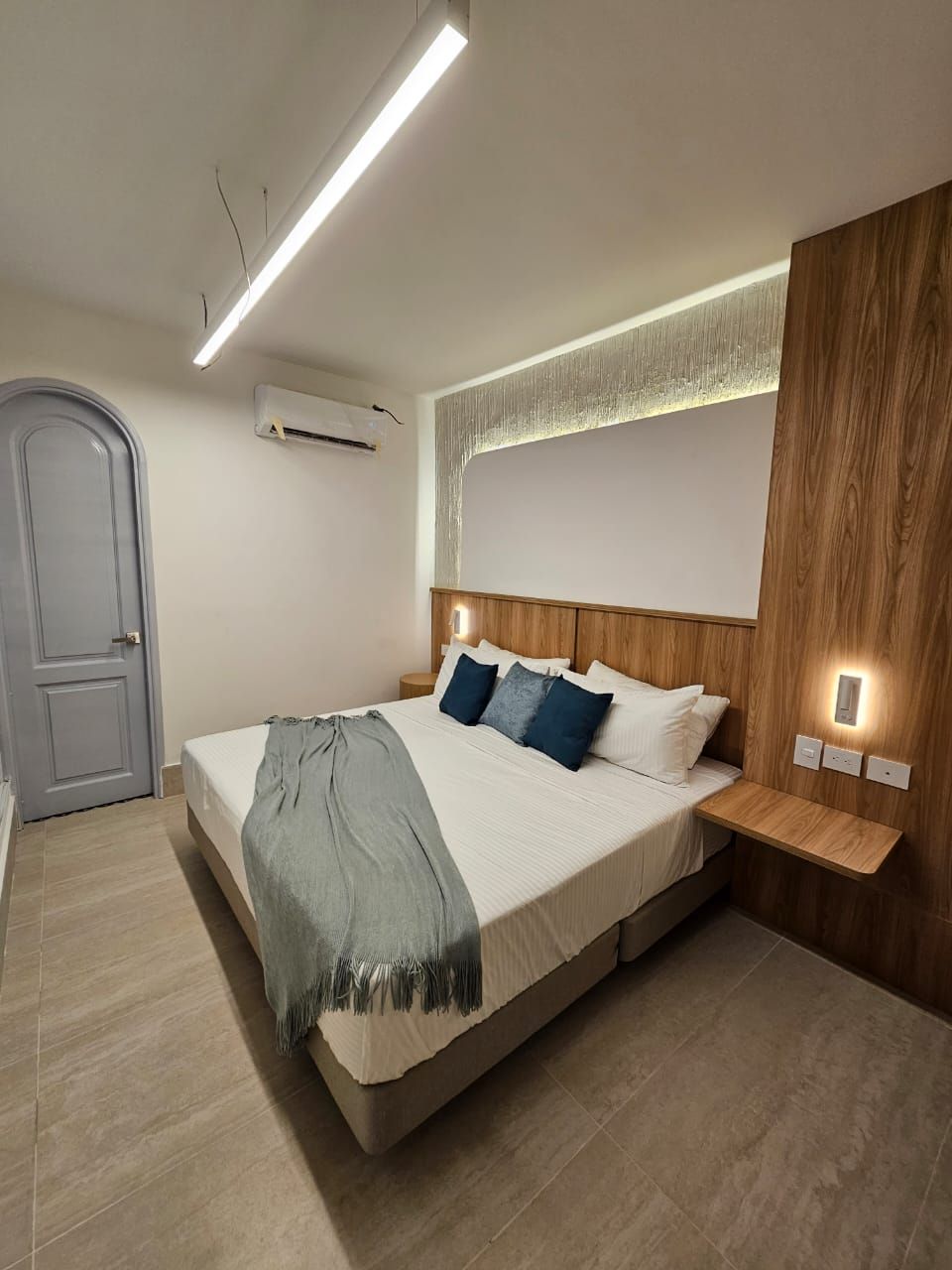 A modern bedroom with a double bed, wooden accent wall, and blue and gray decor.