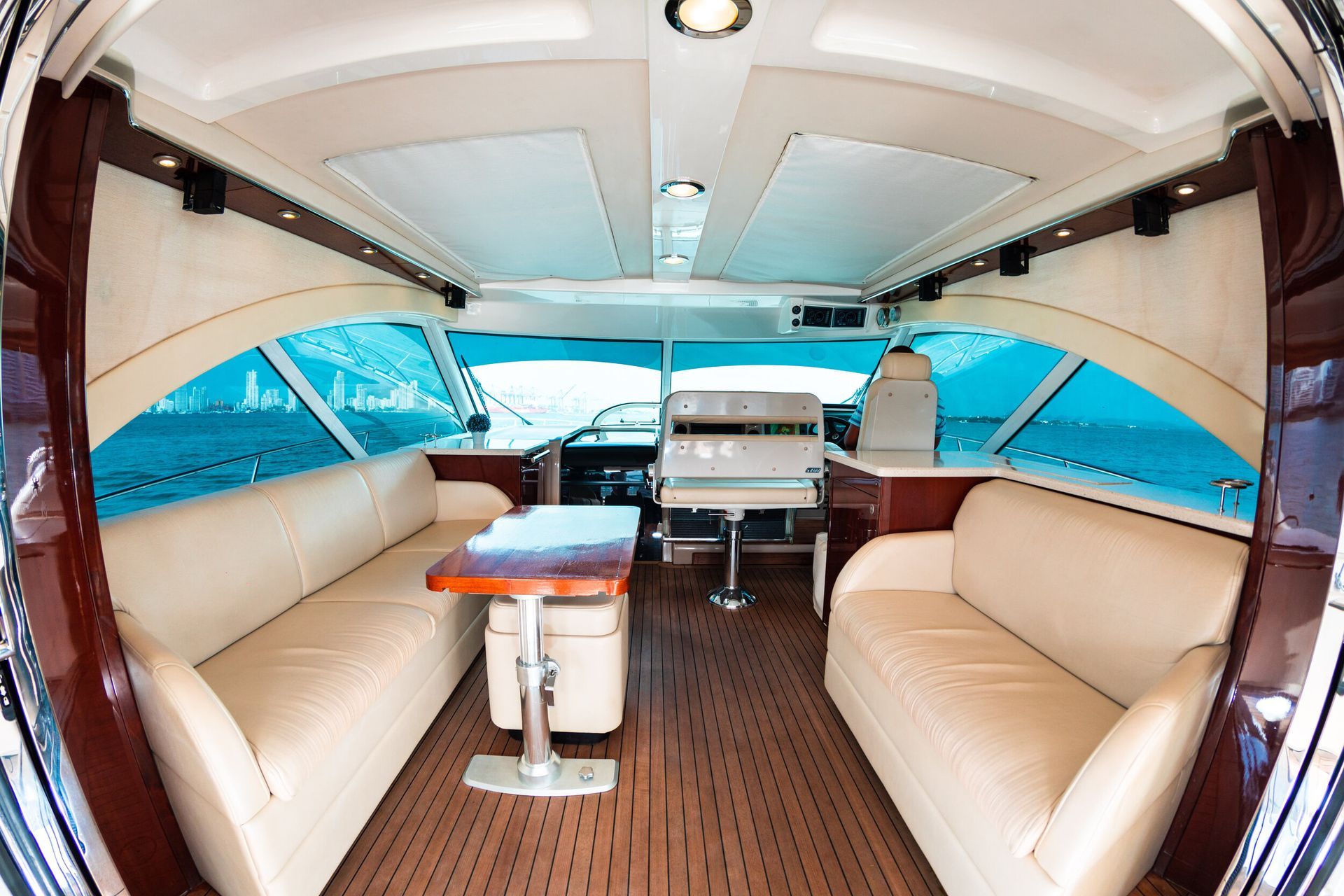 Interior of a yacht with tan leather seating, a wooden table, and large windows overlooking the water.