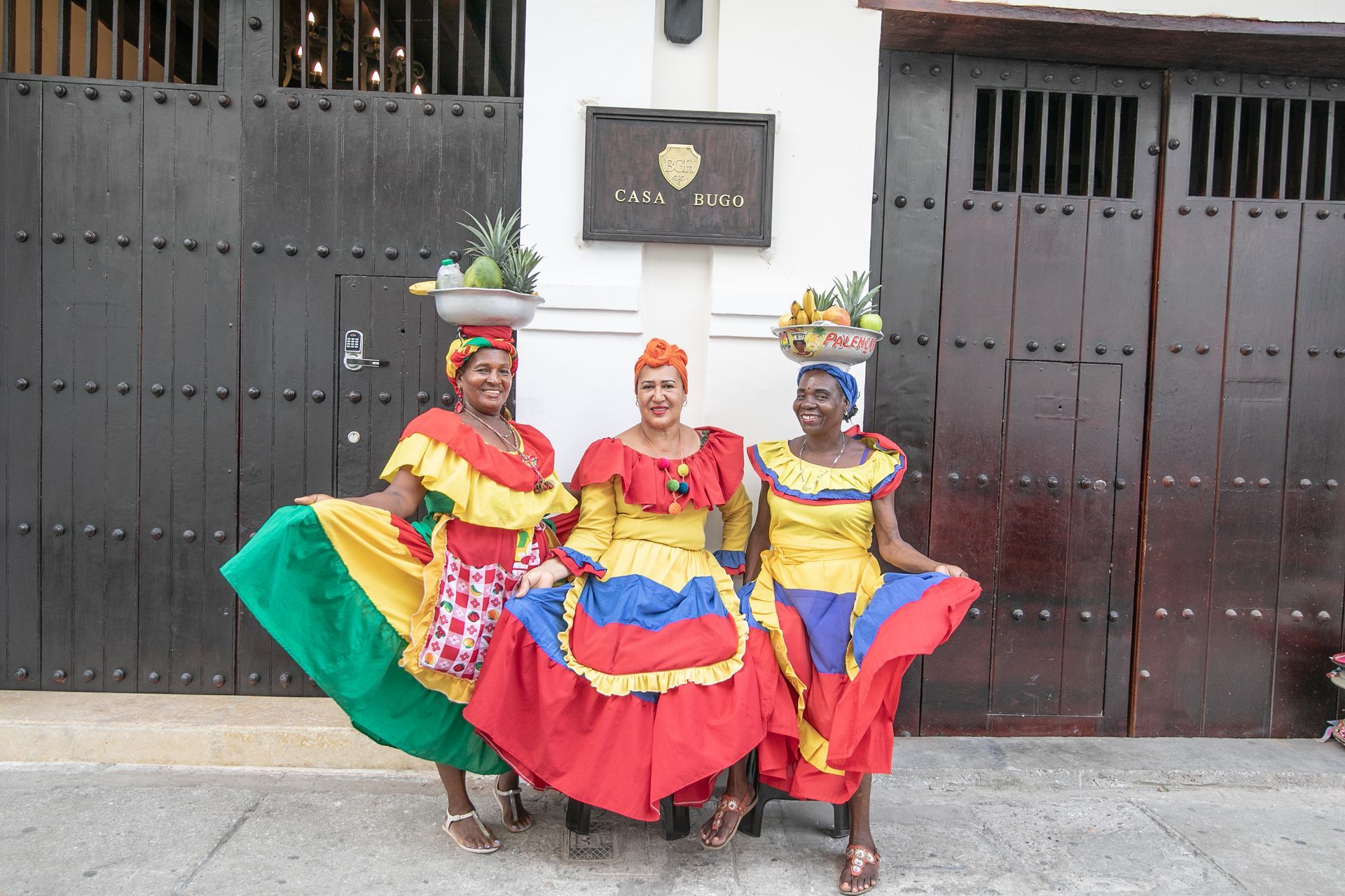 Three women in colorful dresses are posing for a picture in front of a building.
