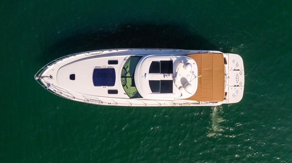 Overhead view of a white yacht on emerald green water, with a tan sun deck and dark blue window panels.