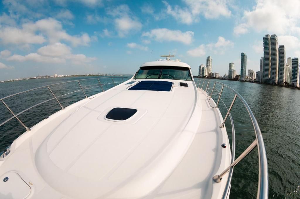 A white yacht sails on blue water towards a city skyline under a partly cloudy sky.