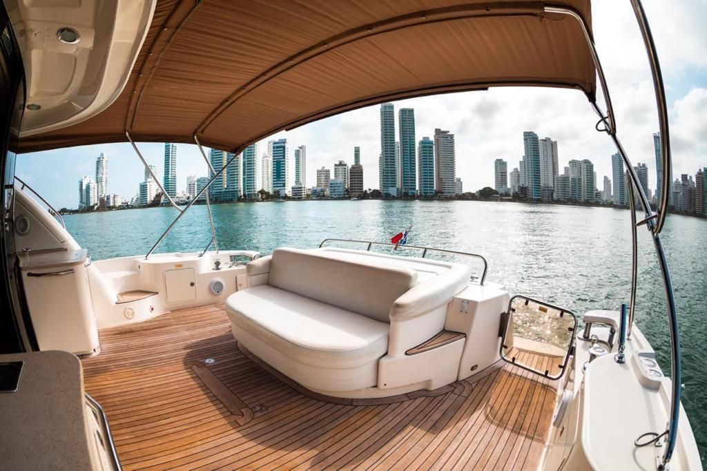 A yacht deck with white seating and a cityscape backdrop under a brown canopy on a sunny day.