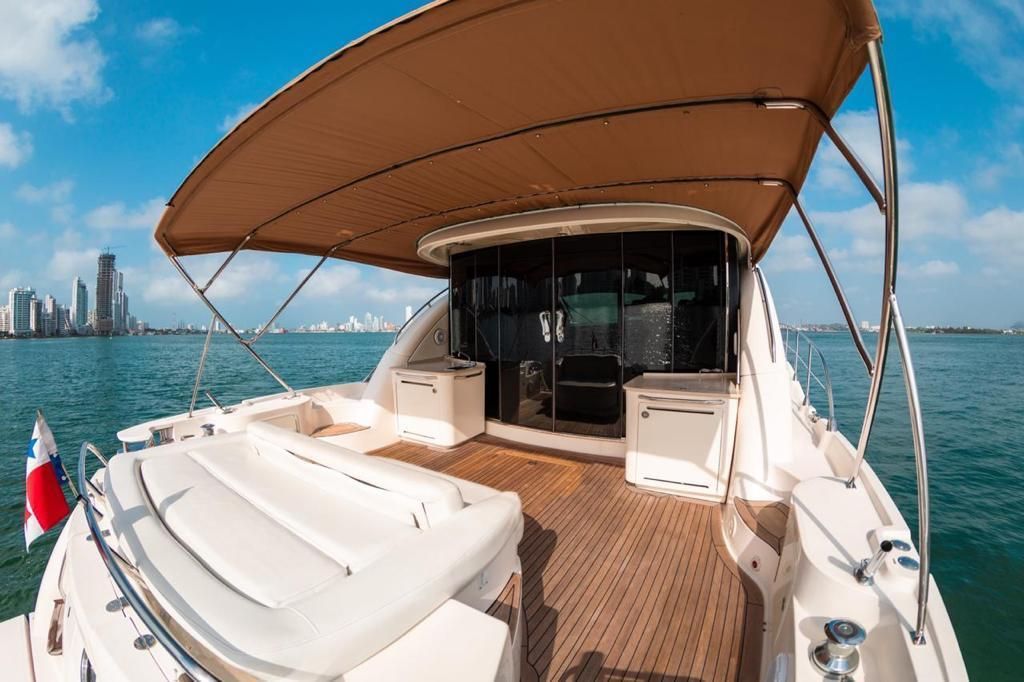 Back of a yacht with a brown sunshade, overlooking a city skyline on a sunny day.