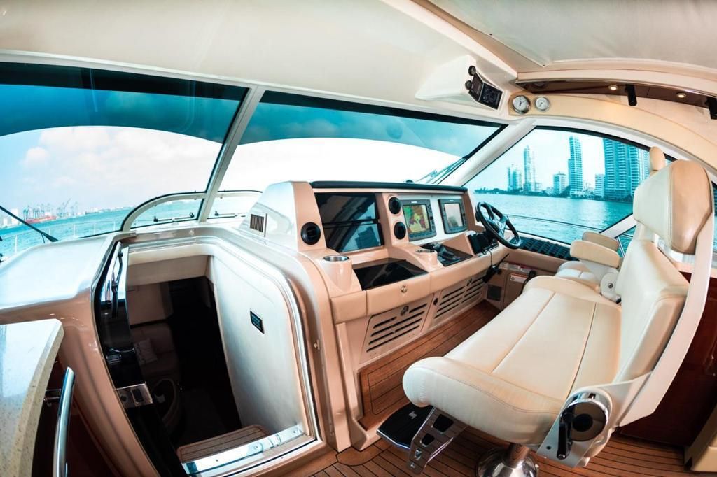 Interior view of a luxury yacht's helm station, featuring a white captain's chair, control panels, and panoramic windows with a city skyline in the background.