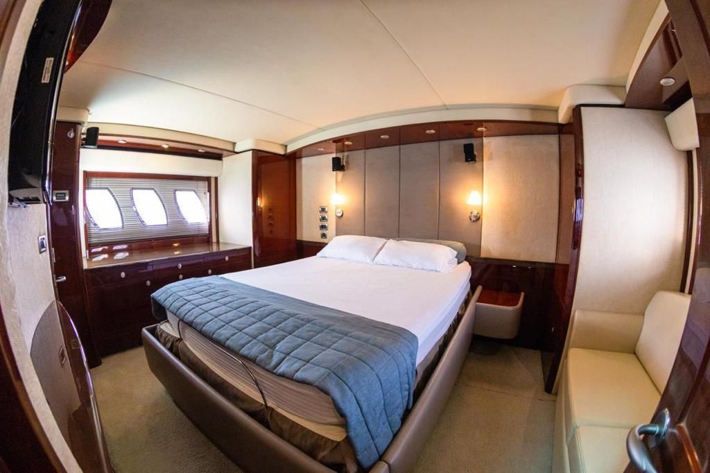 Interior of a luxury yacht bedroom.  A double bed with blue blanket sits in the center, with wood paneling and windows on the walls.