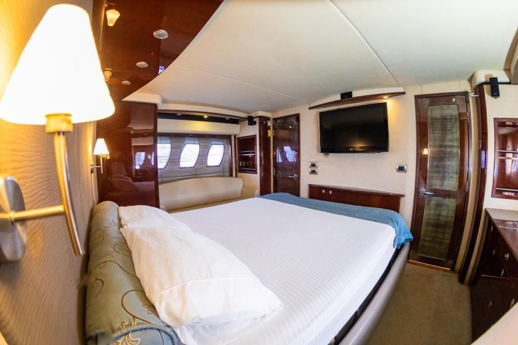Luxurious yacht bedroom with a large bed, TV, and wood paneling. Soft lighting and a cozy atmosphere.
