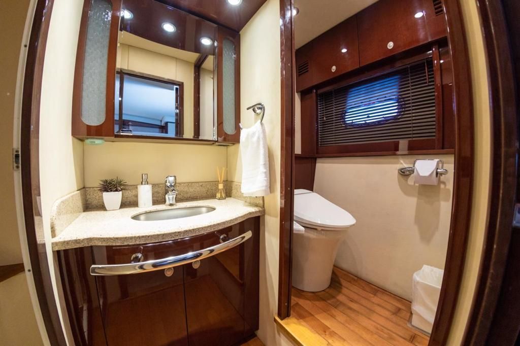 A luxurious bathroom on a boat, featuring a sink, toilet, and wood accents. Beige walls and a window with blinds.
