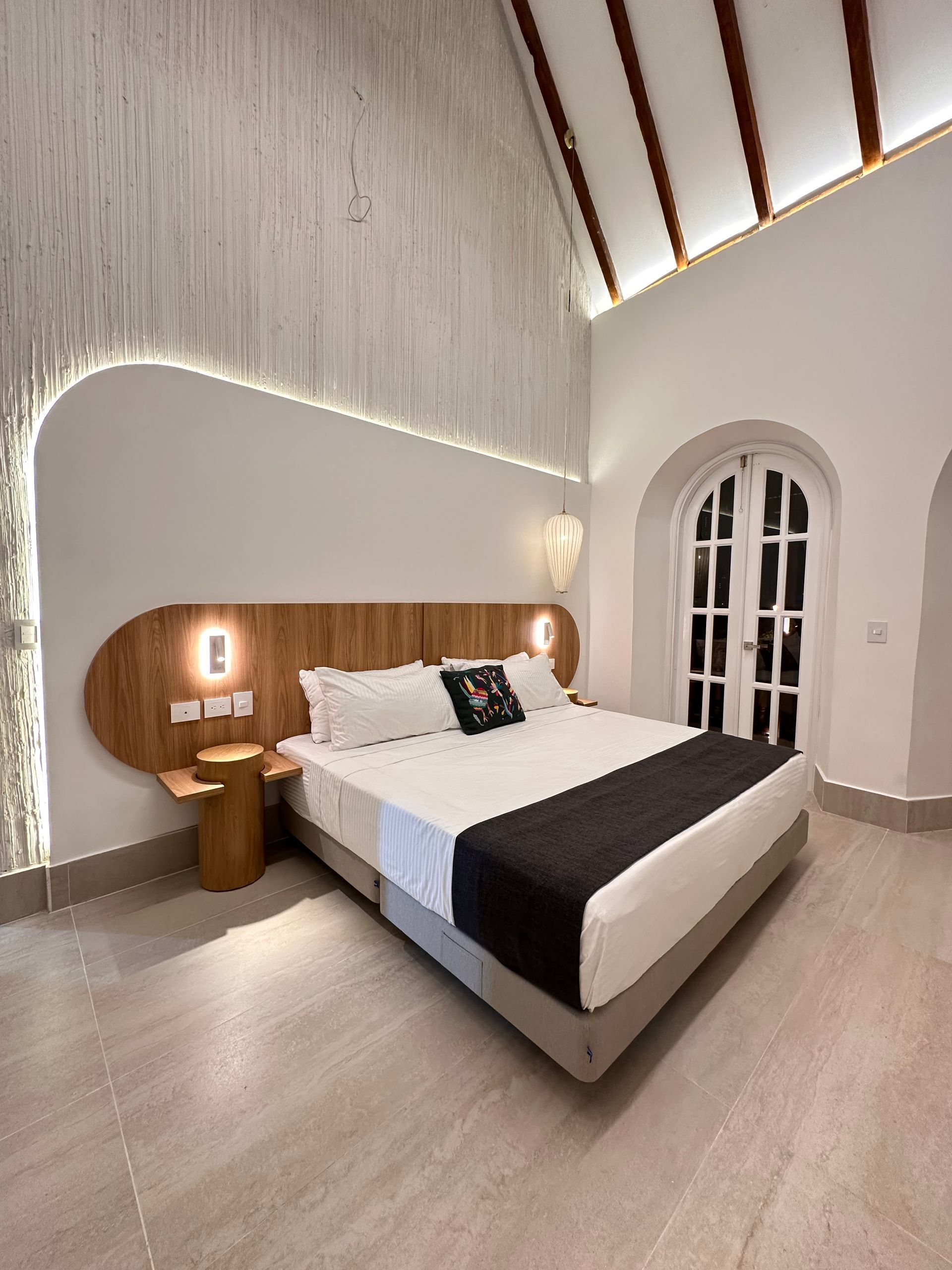 Hotel room with a large bed, wooden headboard, and white walls and arched doorway.