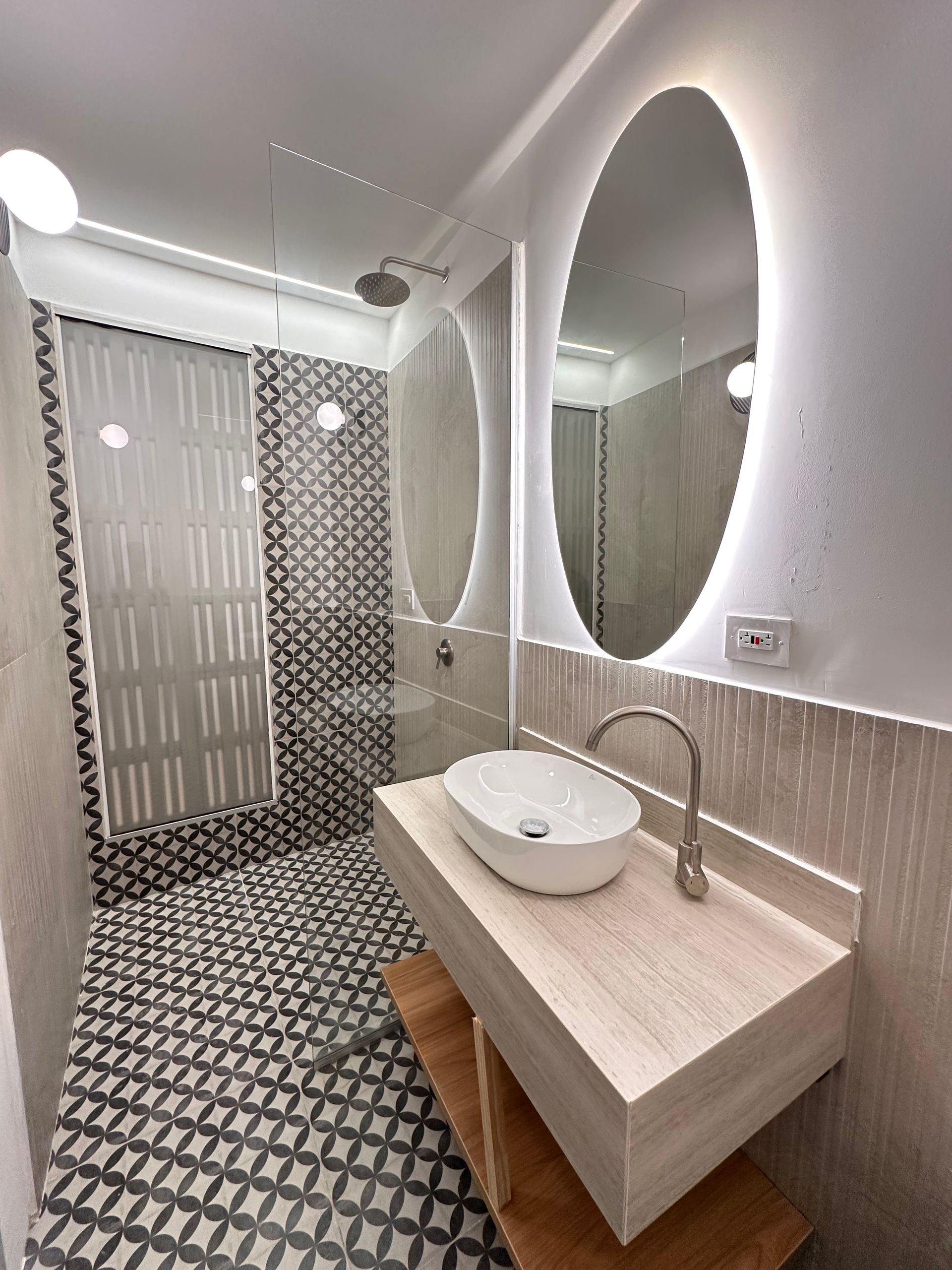 Modern bathroom with patterned floor and shower tiles. Features a floating vanity with a vessel sink, and oval mirrors with backlighting.