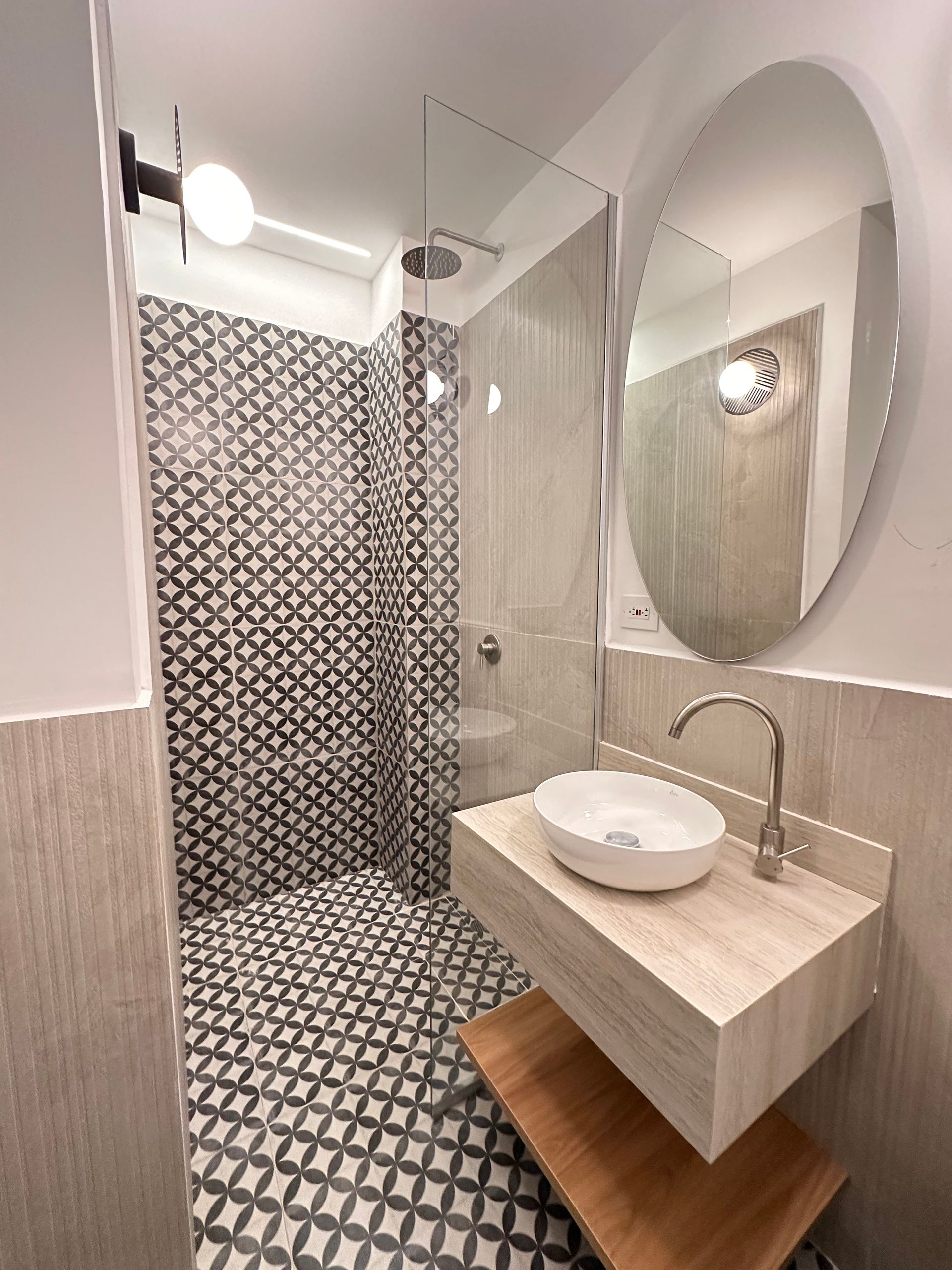 Modern bathroom with patterned tile floor, shower with glass door, floating vanity with a round sink and oval mirror.