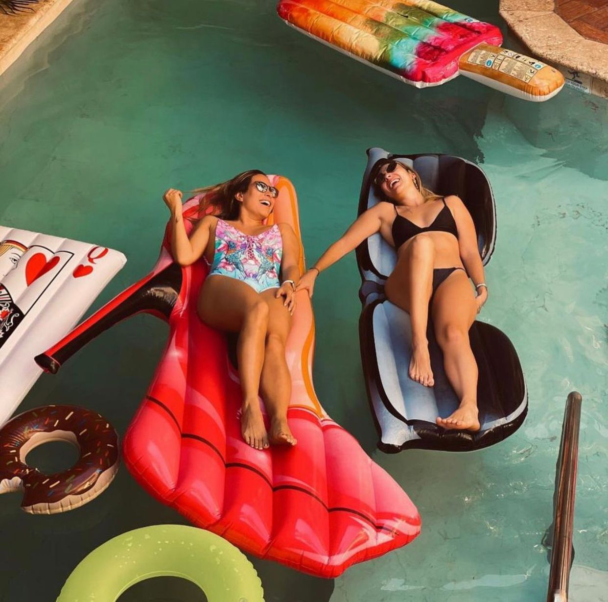 Two women are laying on rafts in a swimming pool