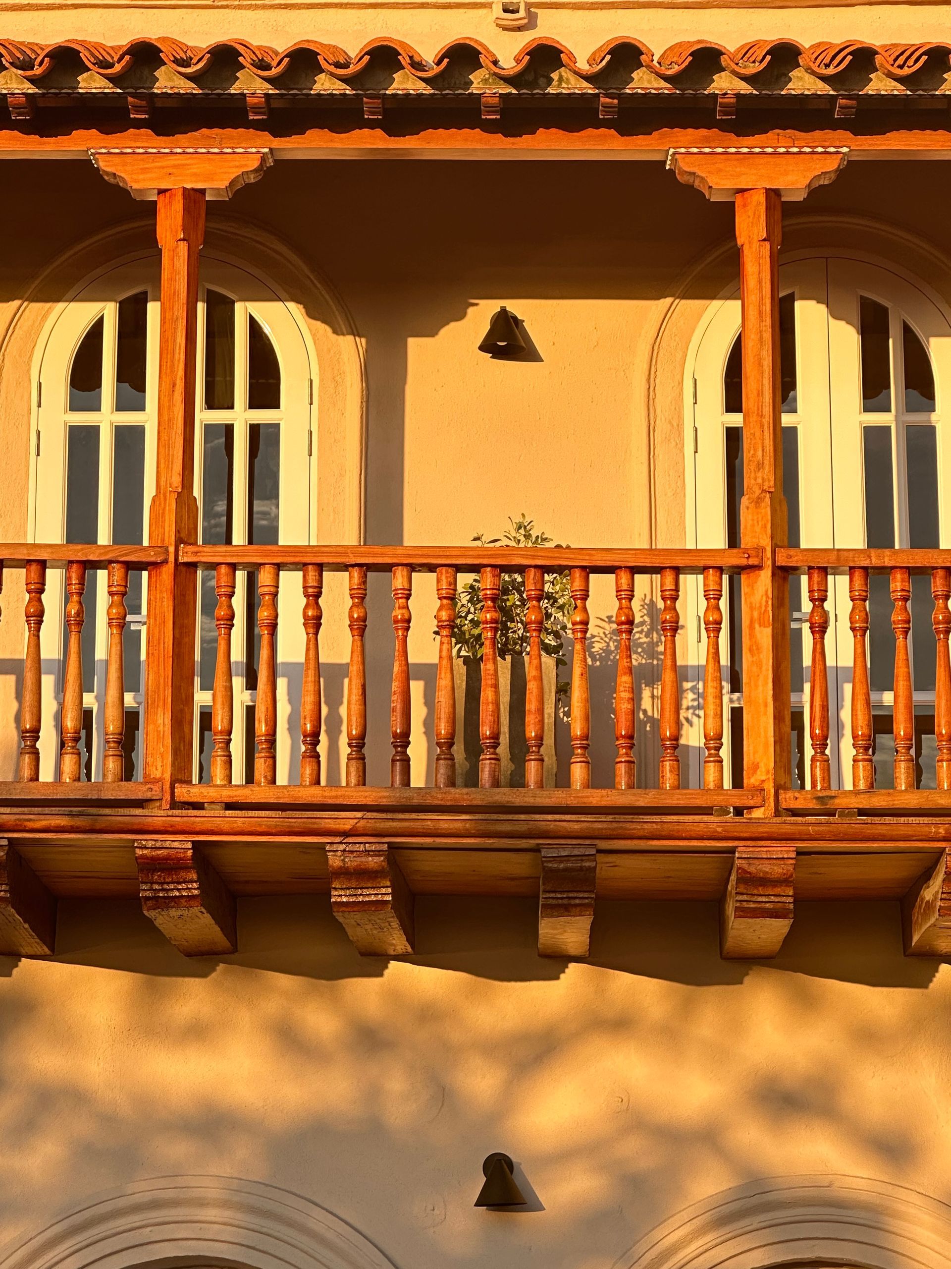 Balcony with arched windows, wooden railing, and decorative trim; bathed in warm sunlight.