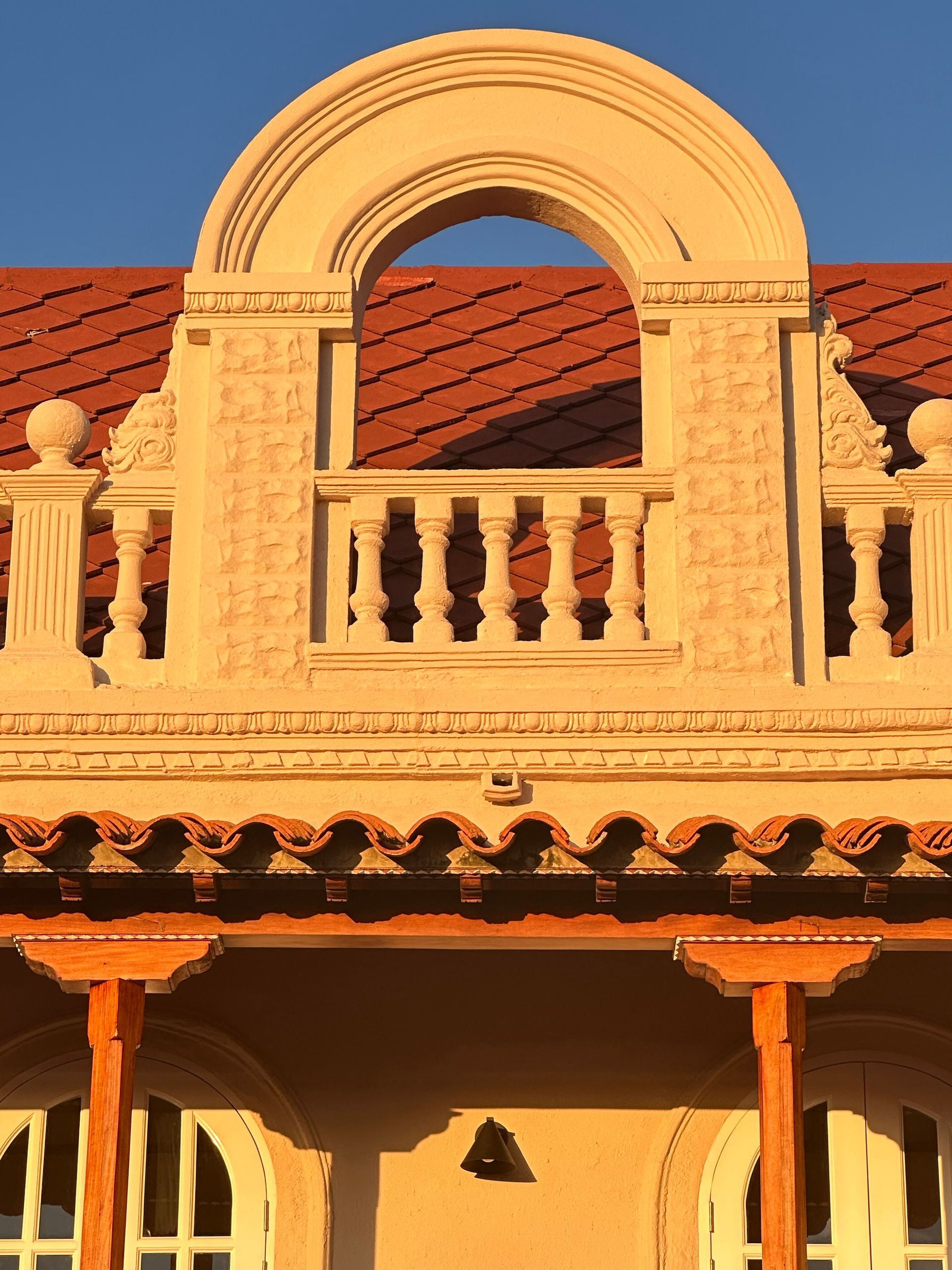 Ornate beige building facade with red tile roof and arched balcony under a blue sky.