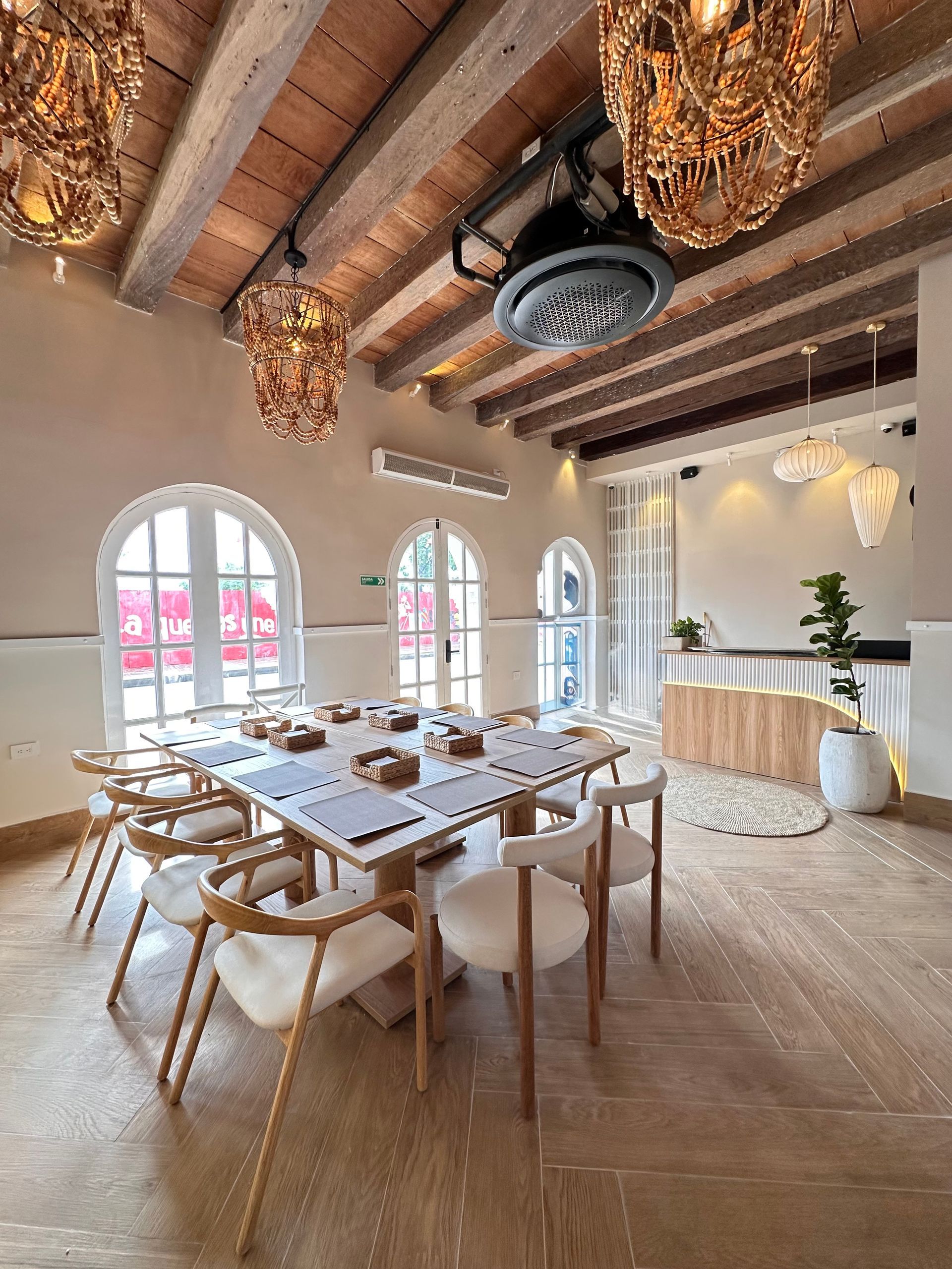 Interior dining room with a large table set for a meal, cream-colored walls, wooden beams, and arched windows.