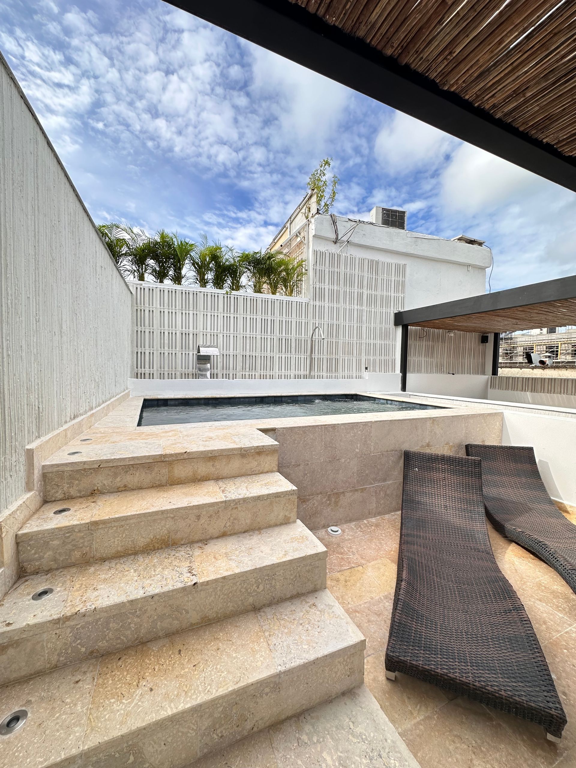Staircase leading down to a small pool and lounge chairs in an outdoor setting with a white fence and cloudy sky.