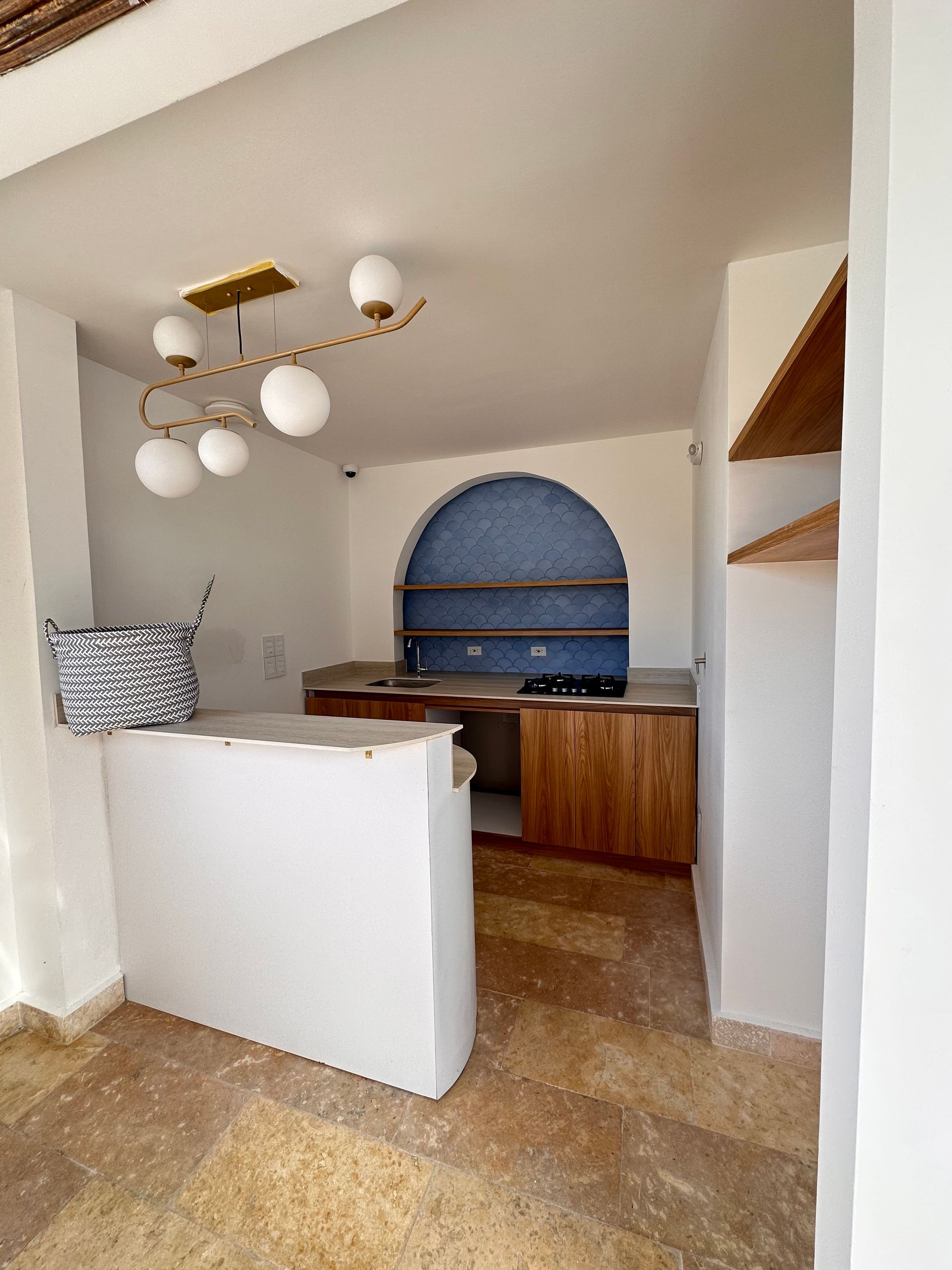 Interior view of a small kitchen area with a white bar, wooden cabinets, and a blue-tiled arch. There is a modern globe light fixture.