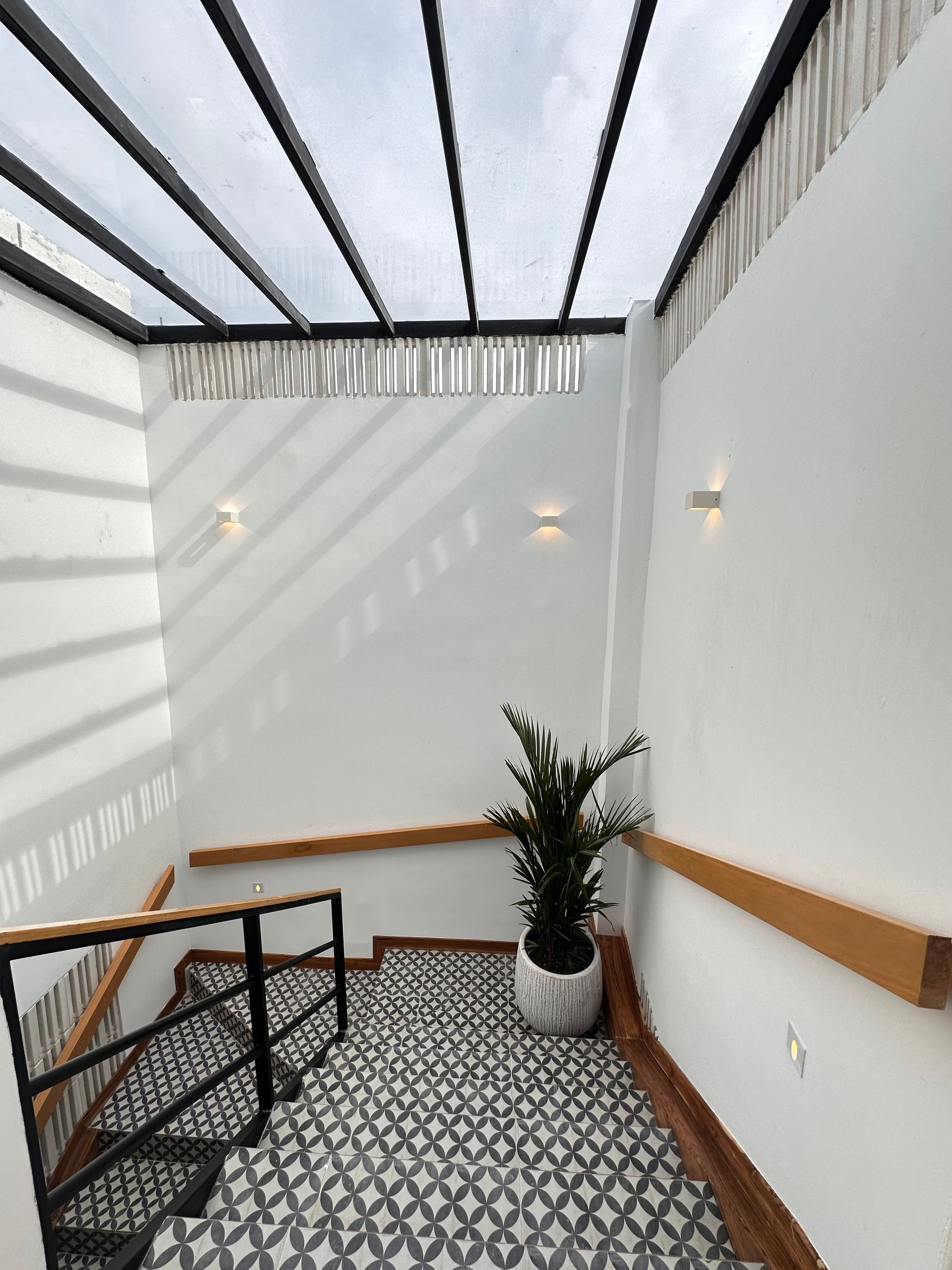 Stairwell with black and white patterned floor, white walls, and a transparent roof. A potted plant sits on the landing.