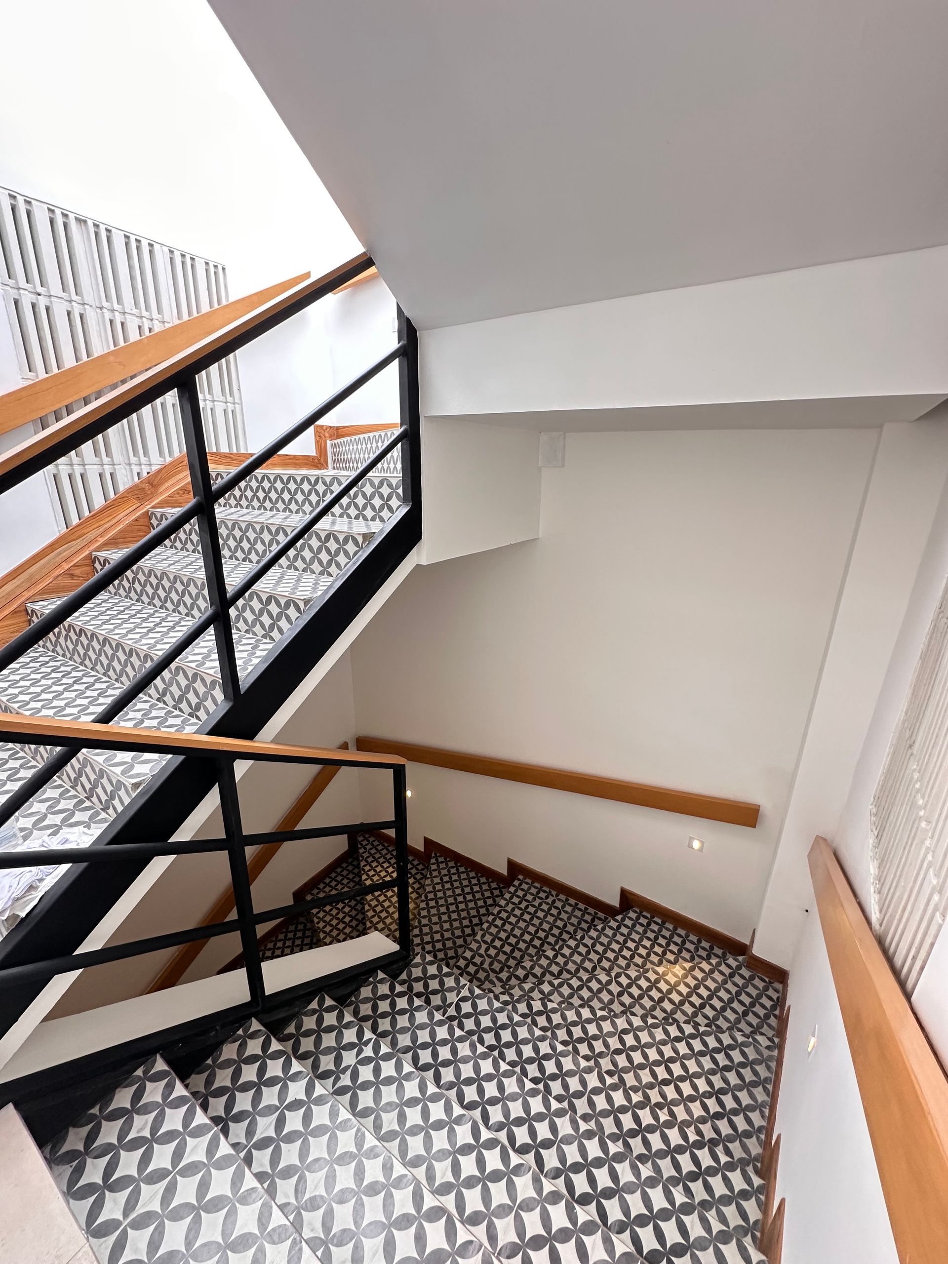 Staircase with black and white patterned tiles, wooden handrails, and black metal railings. The stairs turn halfway down.