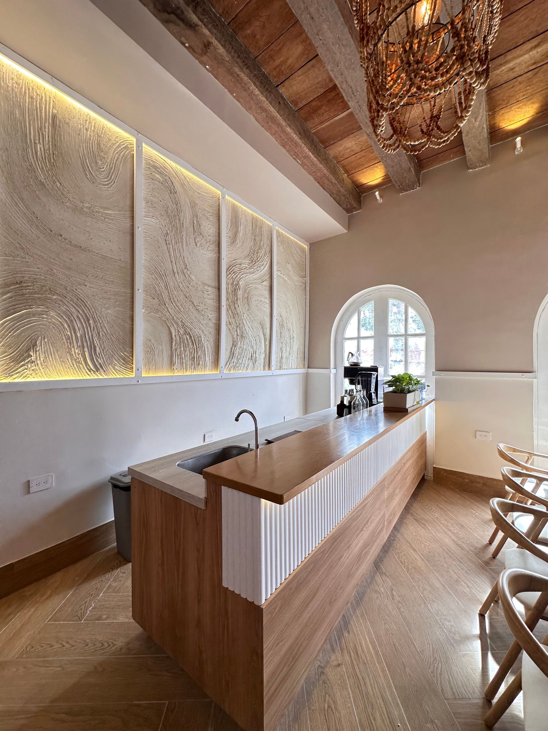 Modern cafe interior featuring a wooden bar with a sink and espresso machine, and abstract wall art, under a beamed ceiling.