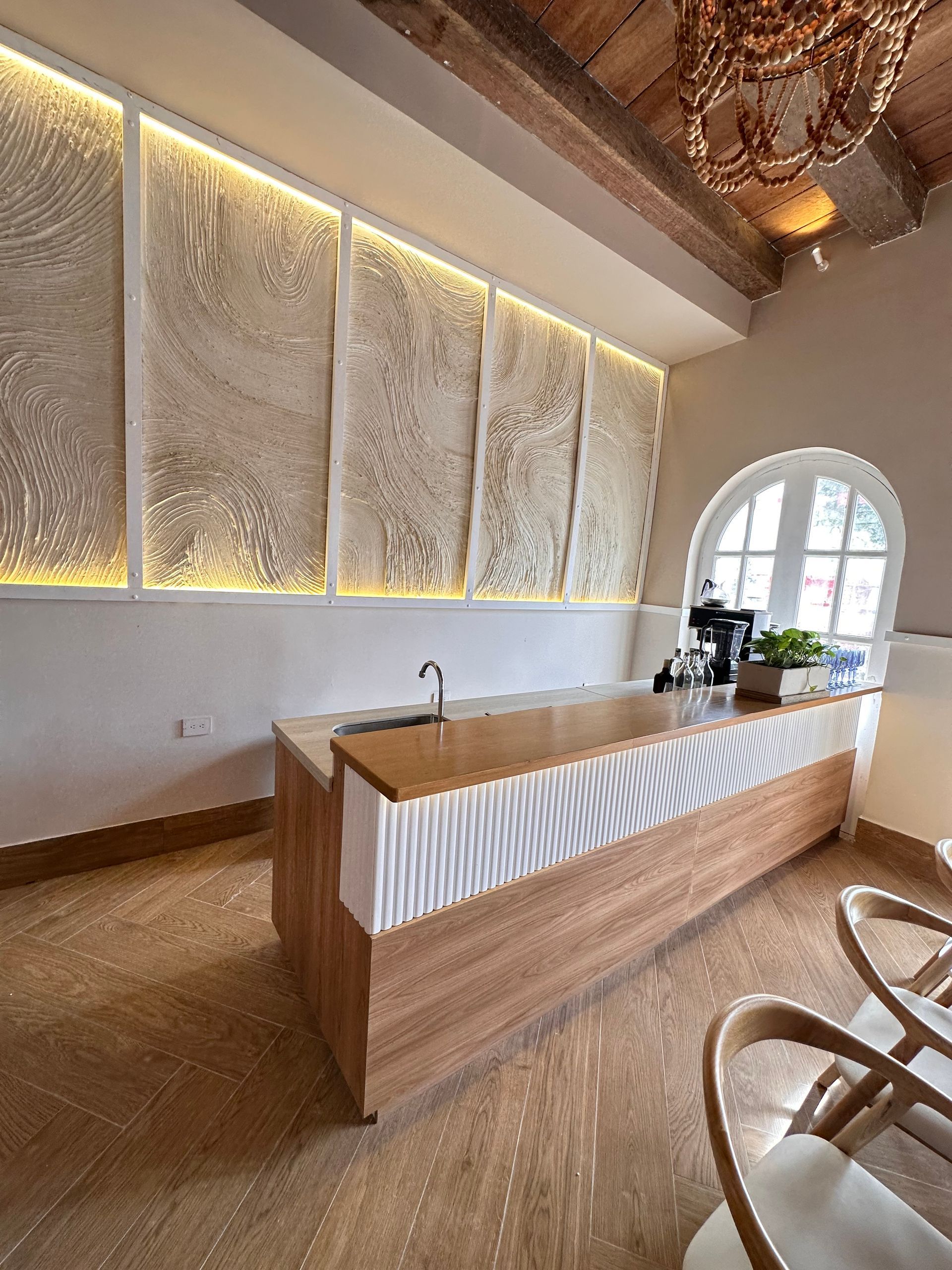 A modern cafe with a wooden counter and textured wall art. The space has a light, airy feel with natural wood tones.