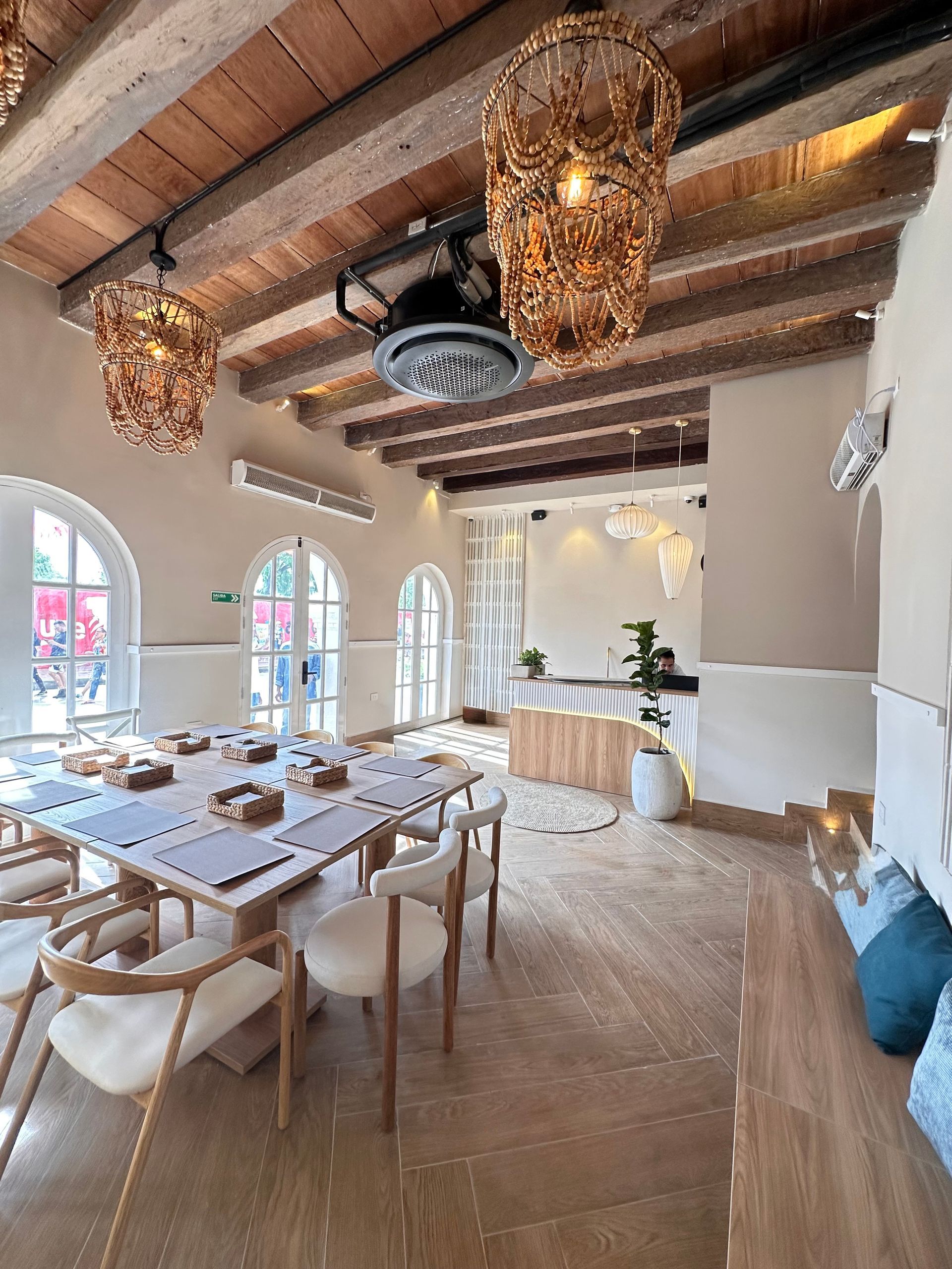 A bright, airy dining room with light wood floors, a long table set for a meal, and decorative pendant lights.
