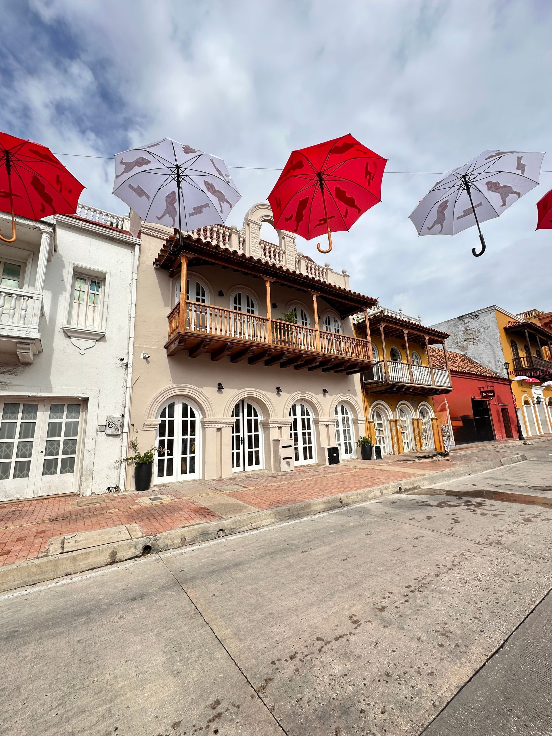 Street scene in Cartagena, Colombia, with colorful buildings and red/white umbrellas suspended overhead.