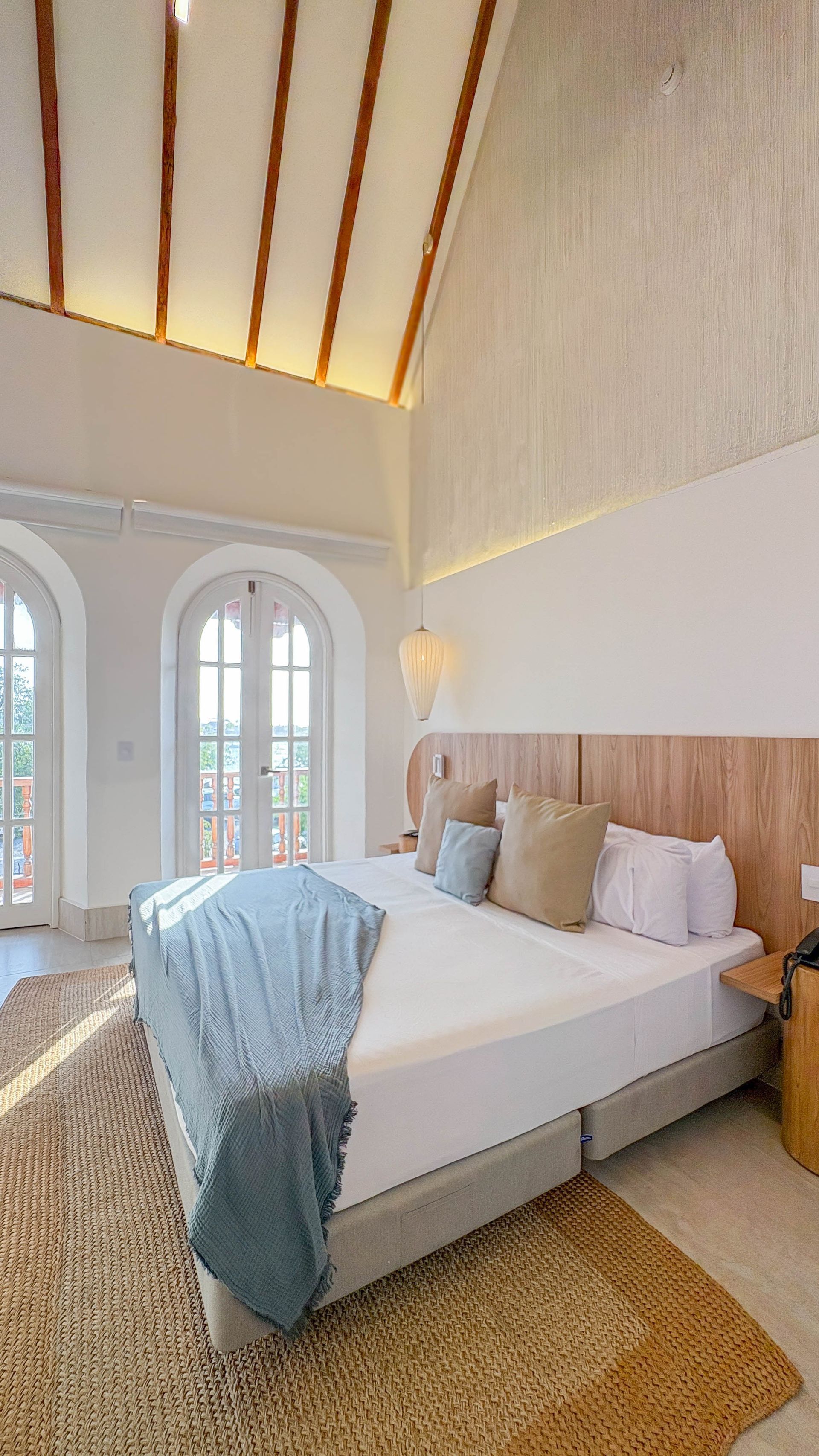 Bedroom with a high, vaulted ceiling, white walls, and a large bed with a wooden headboard. French doors lead to the outdoors.
