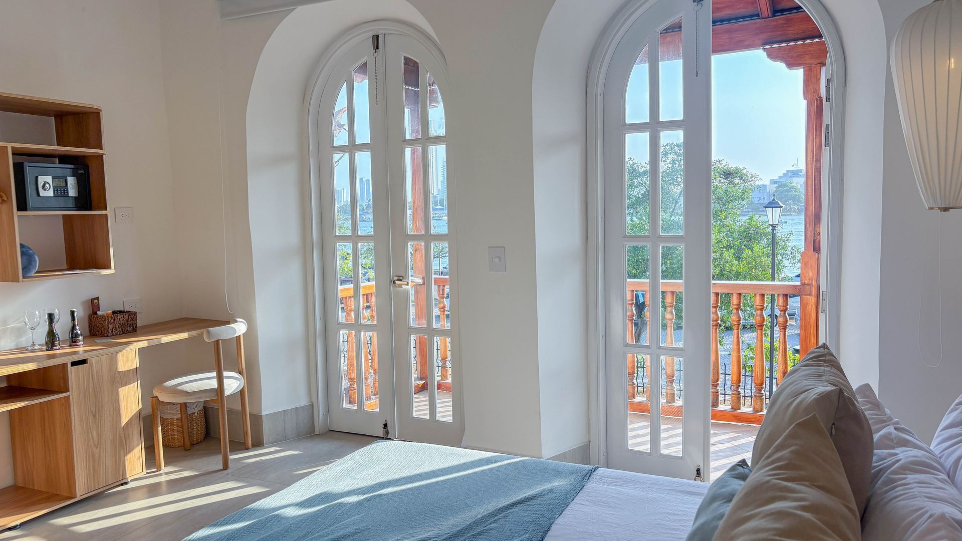 Bright bedroom with arched French doors opening to a balcony. A desk, bed, and shelving are visible.