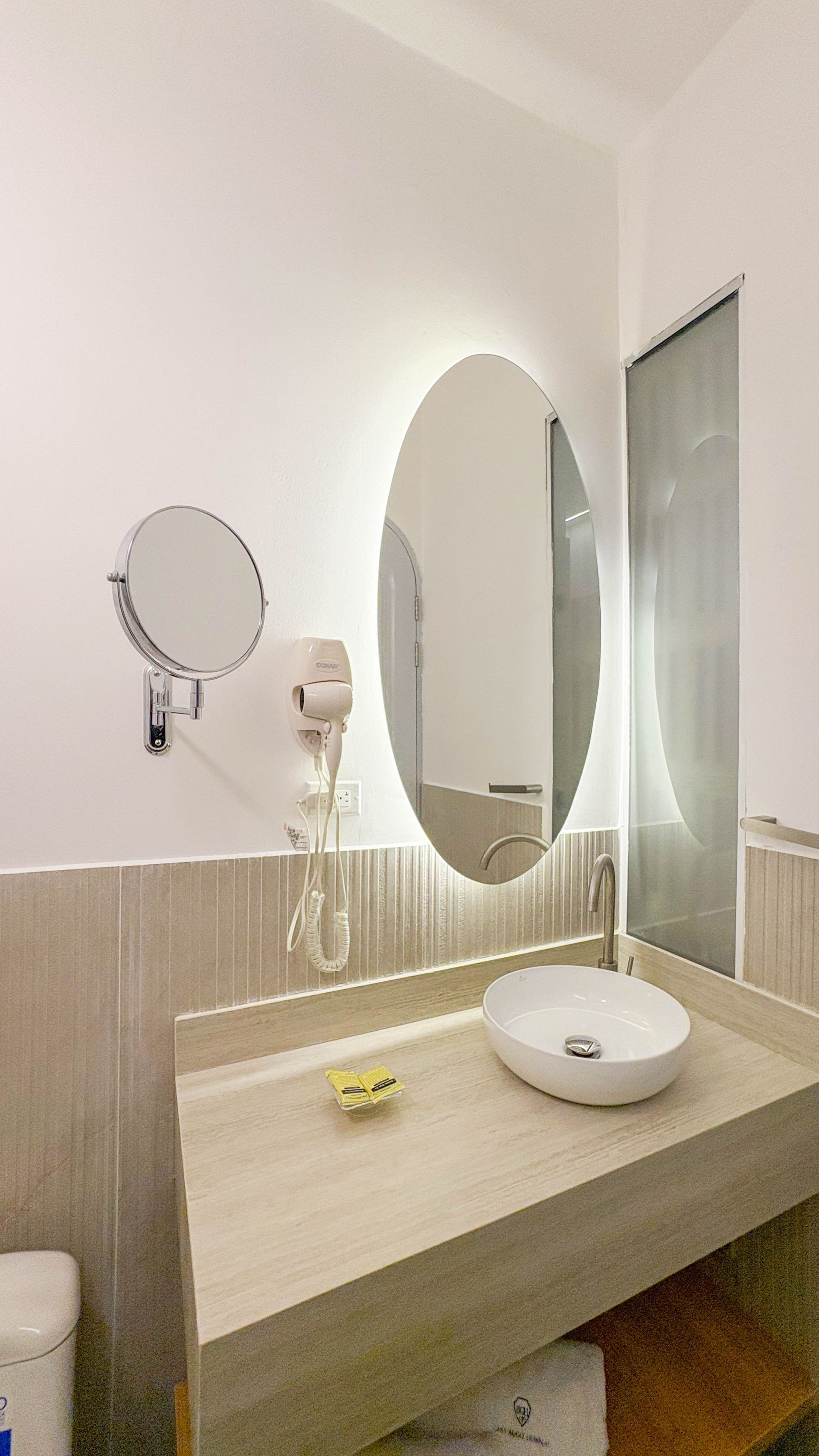 Bathroom with a white sink, oval mirror, and a hairdryer mounted on a light-colored counter.