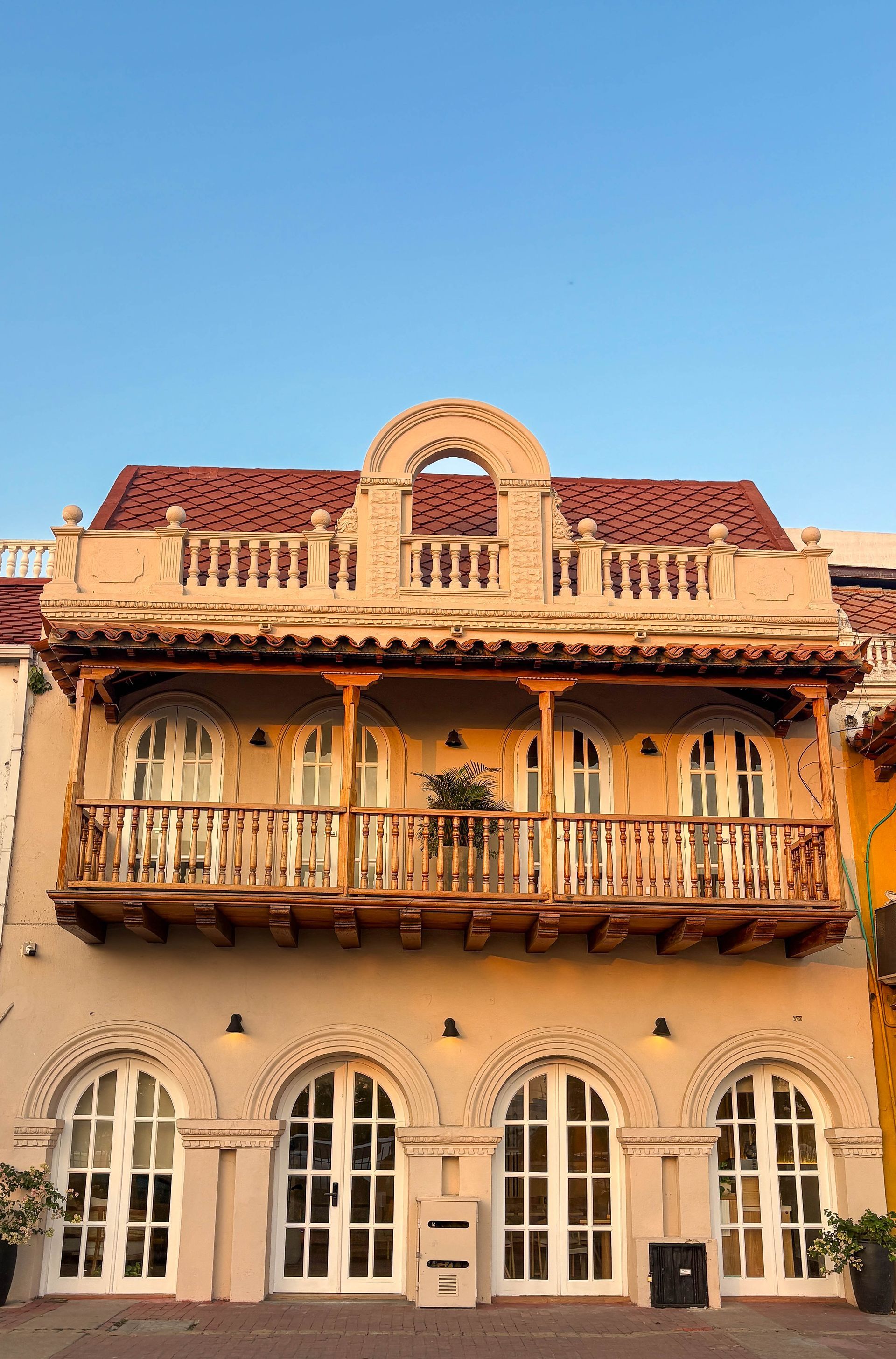Historic building with arched windows and a wooden balcony, bathed in sunlight against a blue sky.