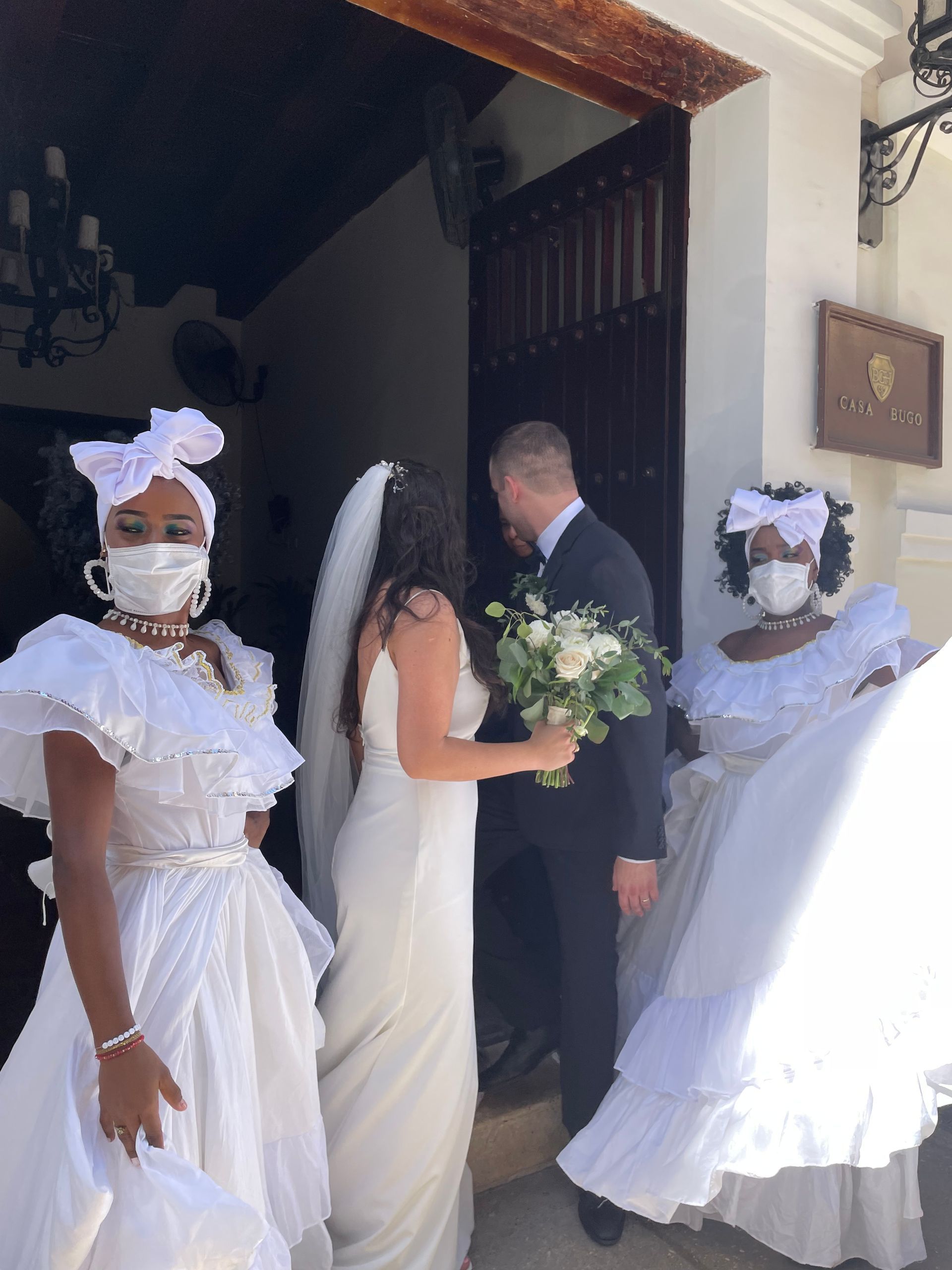 A bride and groom wearing face masks are walking out of a church