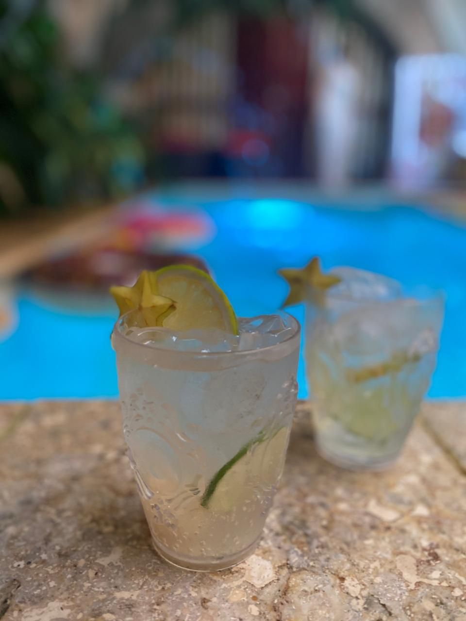 Two glasses of drinks are sitting on a table next to a pool.