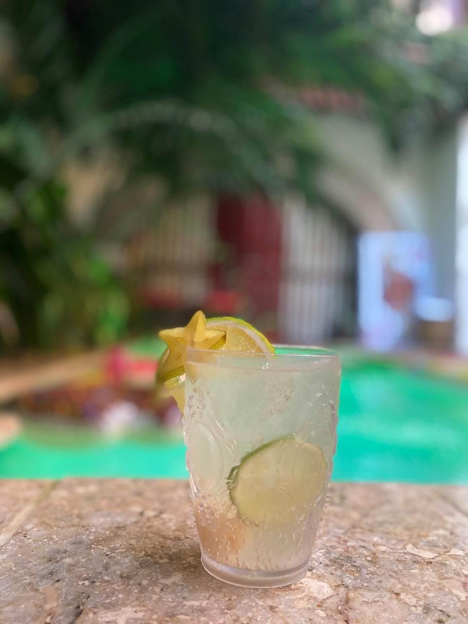 A glass of lemonade with a slice of lemon on top is sitting on a table next to a pool.