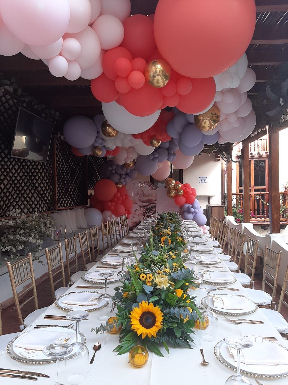 A long table with plates and glasses and balloons hanging from the ceiling