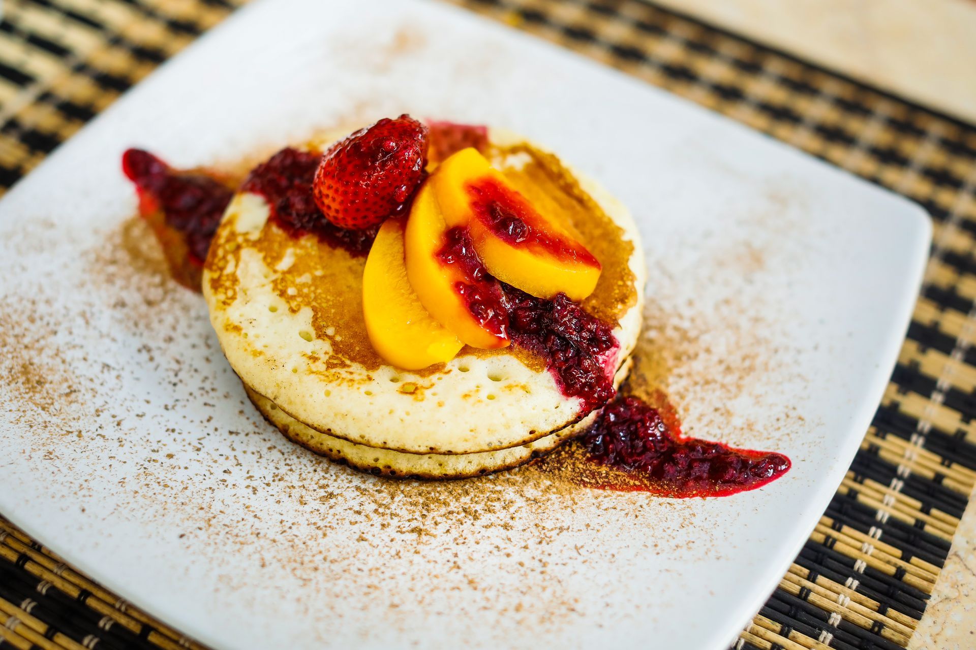 A white plate topped with pancakes and fruit on a table.