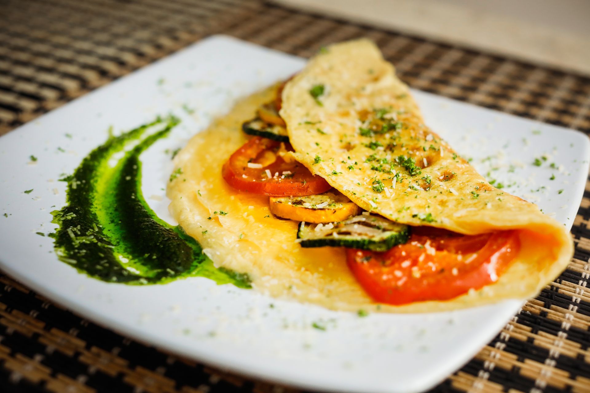 Omelet with grilled vegetables, served on a white plate with pesto sauce.