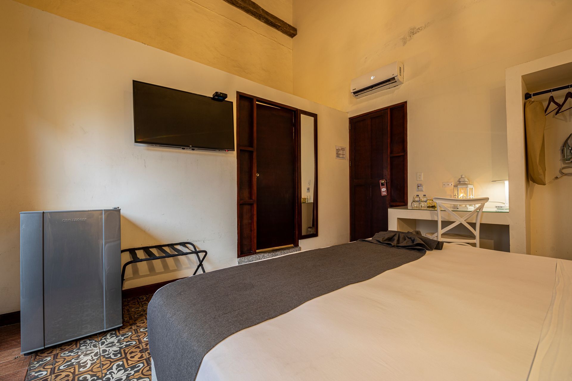 A hotel room with a bed , desk , television and a refrigerator.