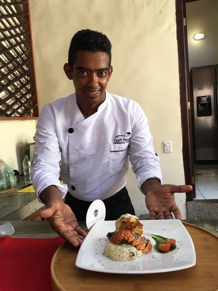 Chef presenting a plate with lobster and rice in a kitchen, smiling.