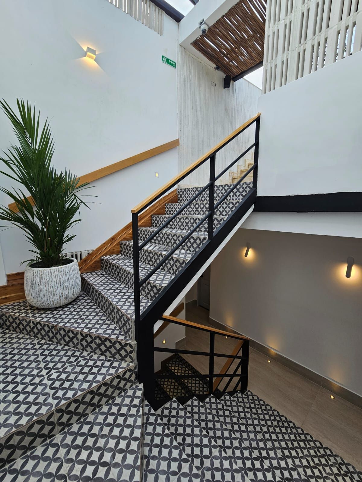 Interior staircase with black and white patterned tiles, black metal railings with wooden handrails, and a potted plant.