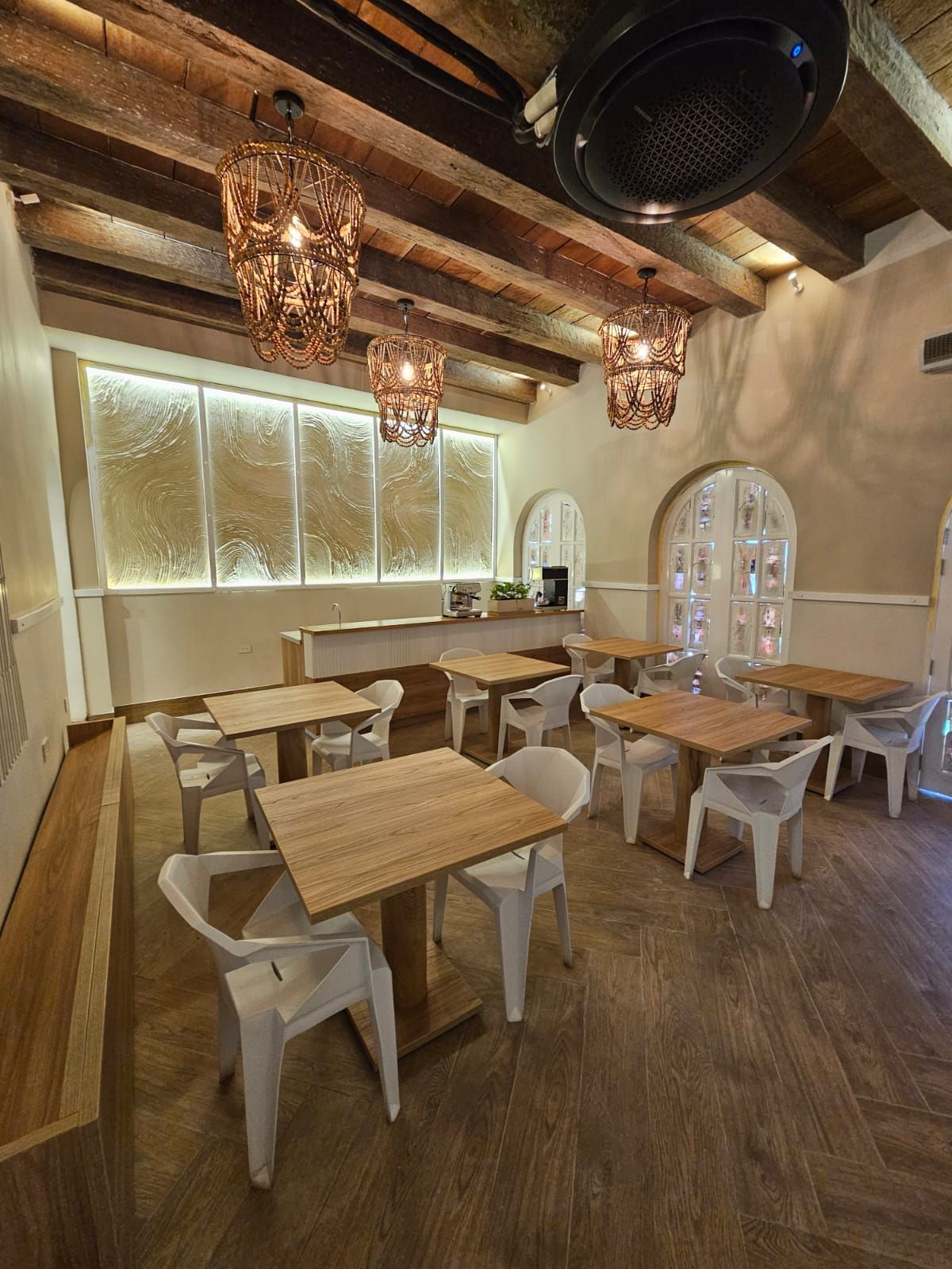 An empty cafe interior with white chairs and wooden tables under decorative hanging lights.