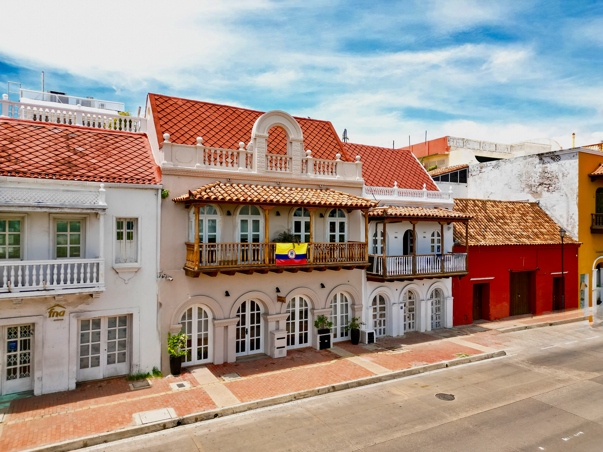 Row of colorful colonial buildings in Cartagena, Colombia, with white, red, and yellow facades under a bright blue sky.