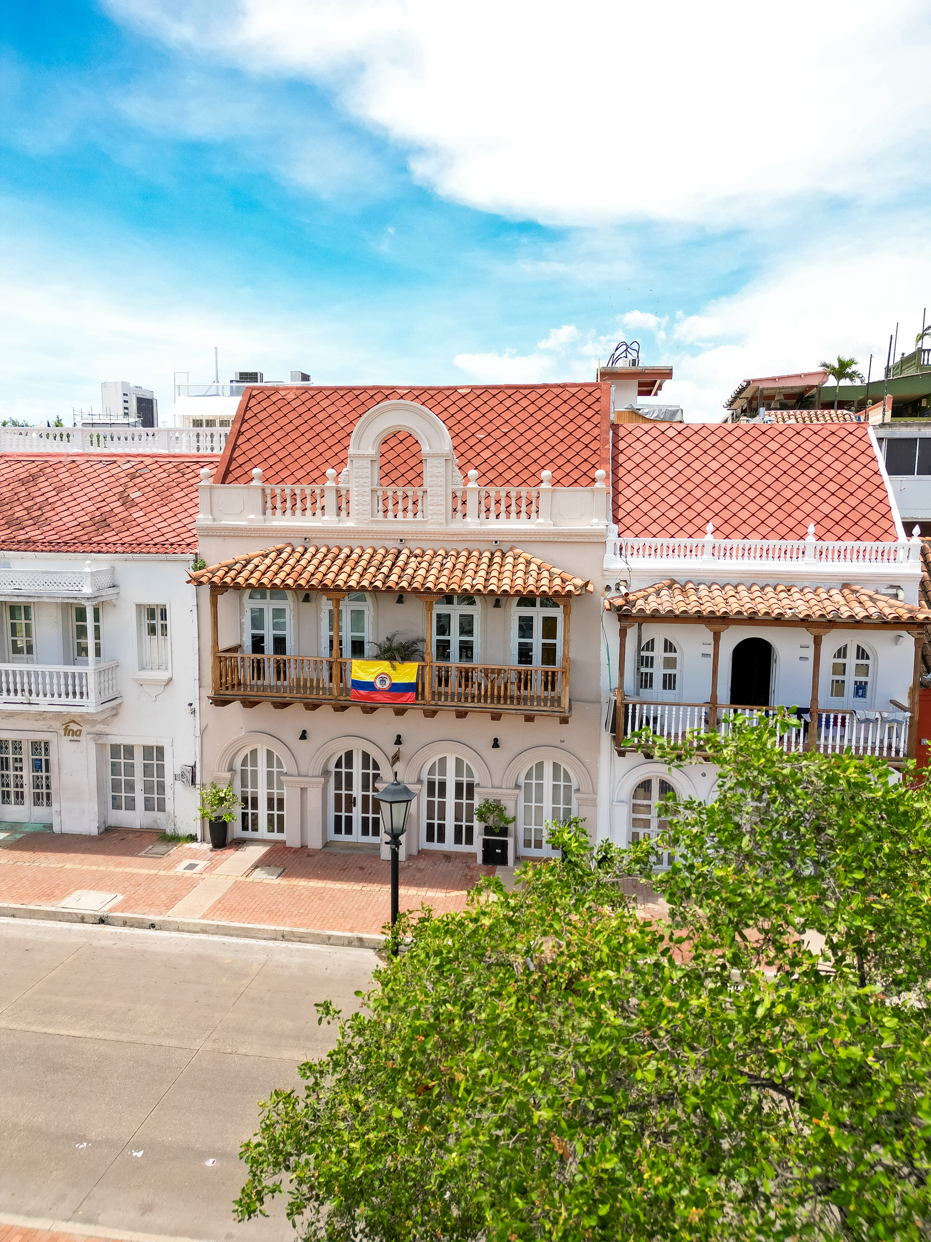White colonial buildings with red tile roofs, adorned with balconies and windows, in Cartagena, Colombia, with a Colombian flag.