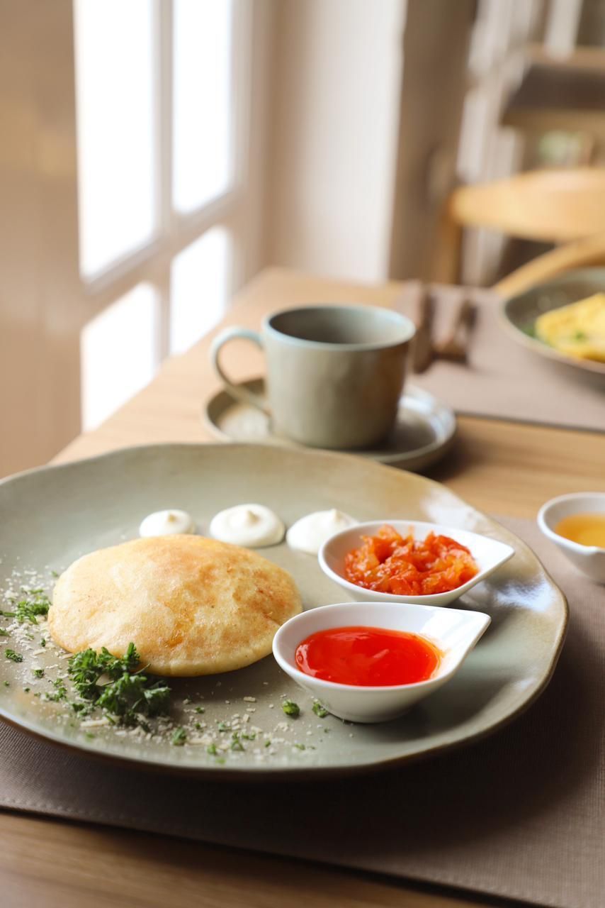 A plate with a puffy bread item, various sauces, and a coffee cup on a table in a cafe setting.