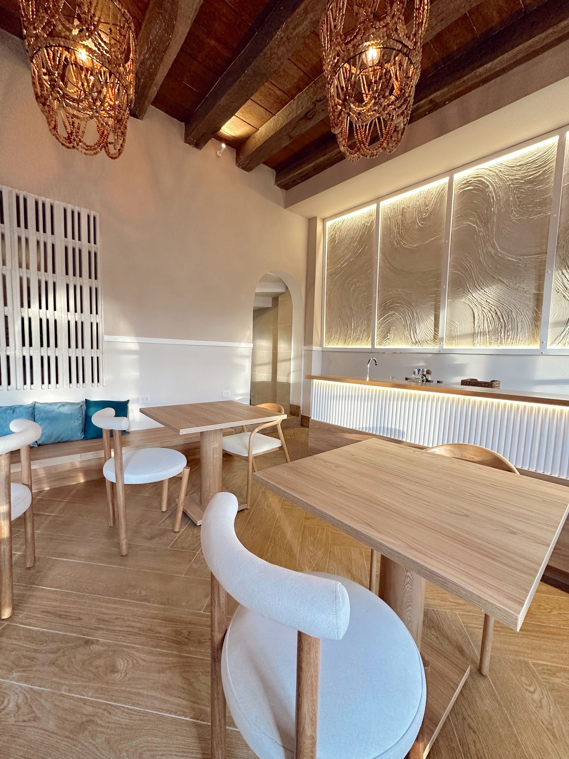 Cozy interior of a cafe with light wood tables, white chairs, and decorative lighting. Soft lighting and neutral tones create a relaxing atmosphere.