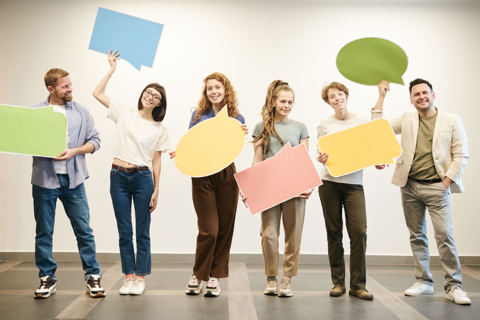 Group of people holding colorful blank speech bubbles in a bright studio, smiling and standing together