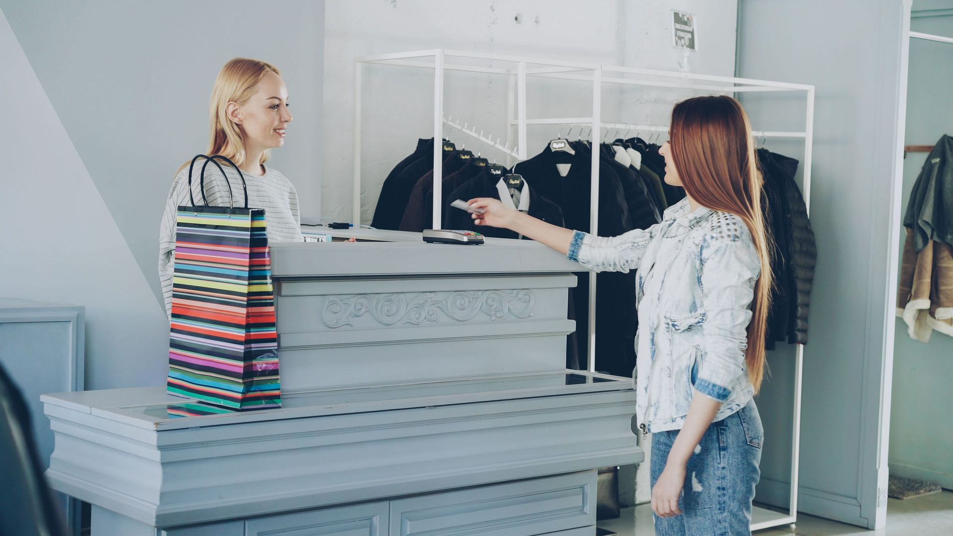 Two people browsing clothes in a bright retail store, one gesturing toward a display rack.