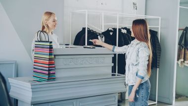 Two people browsing clothes in a bright retail store, one gesturing toward a display rack.